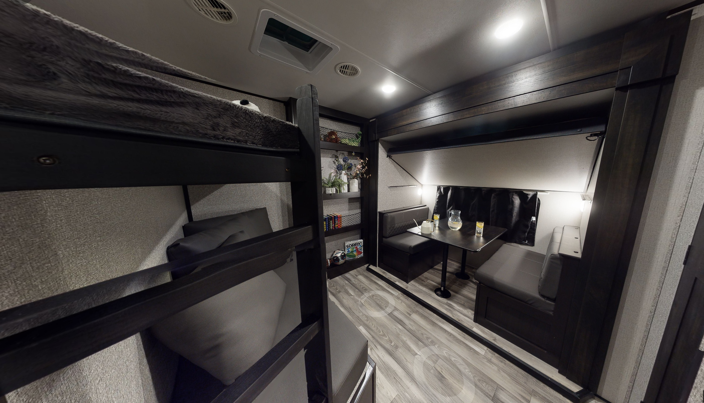 Modern RV rental interior featuring dark wood bunk beds and a light grey dinette with a table. Perfect for family travel.. Highland Ridge RV Mesa Ridge 2022
