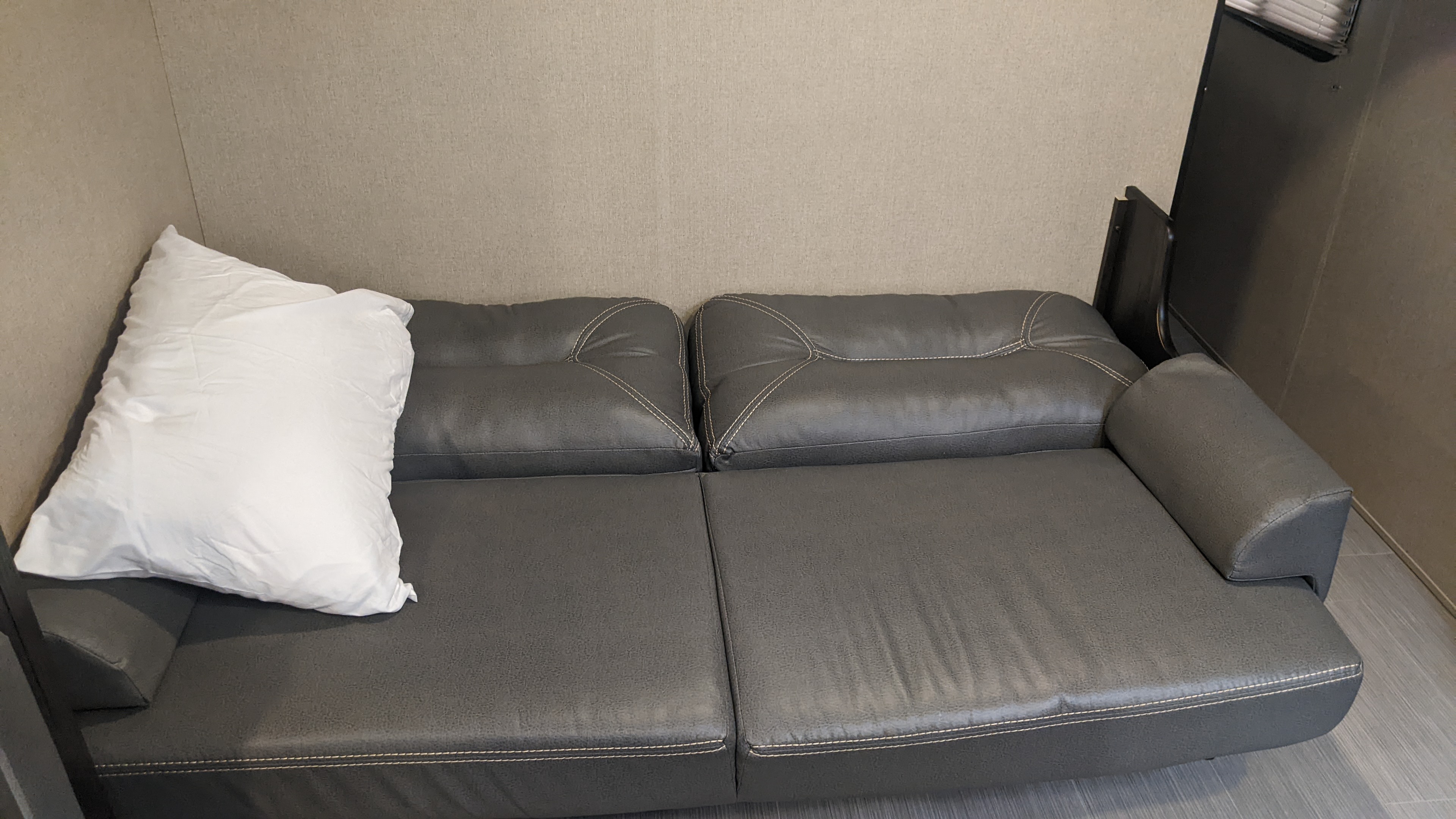 Interior view of an RV rental showing a comfy grey leather sofa with white stitching and a white pillow.. Dutchmen Kodiak Express 2017