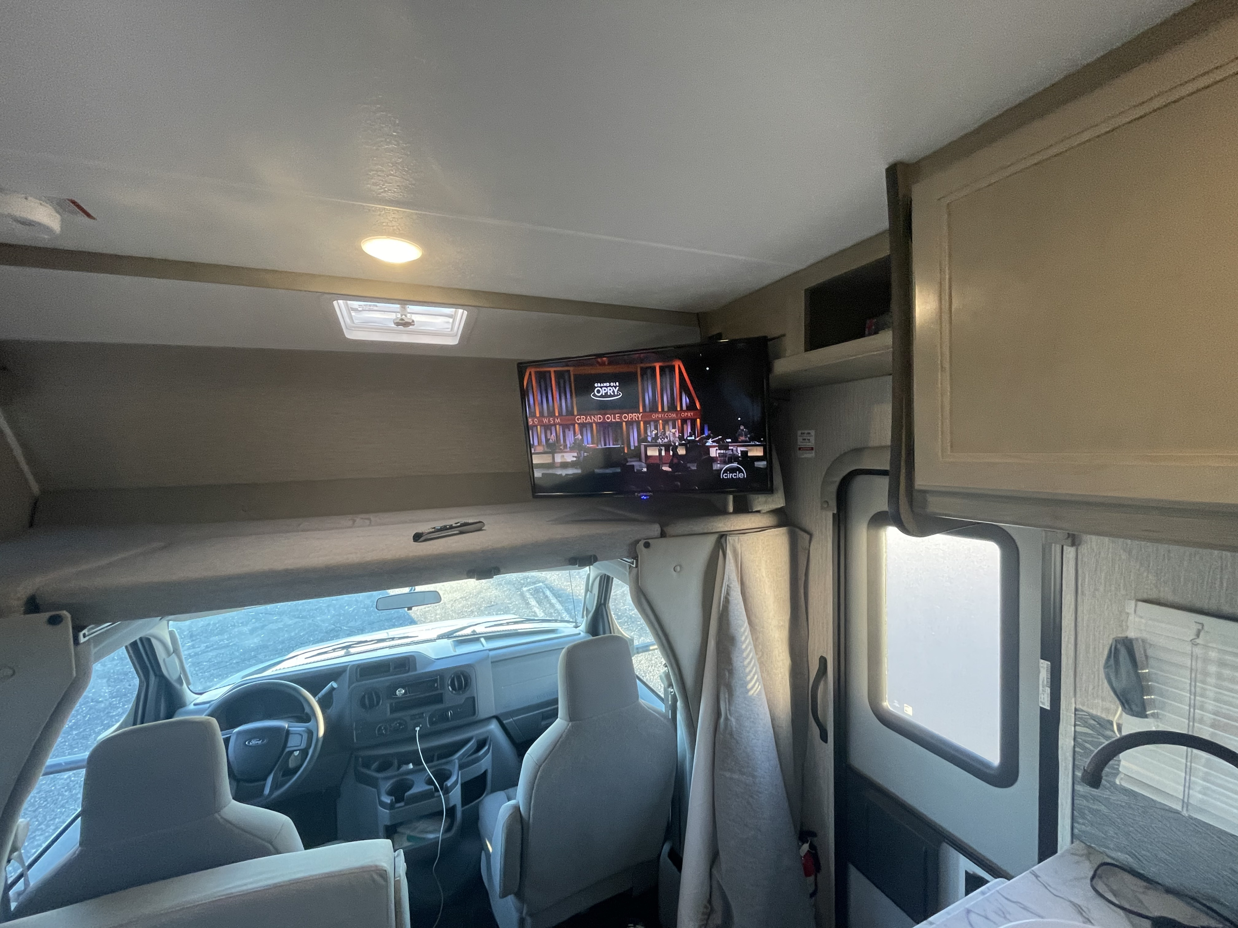 Inside a spacious RV rental, with a view of the front cab, overhead bunk, and mounted TV, perfect for travel comfort.. Forest River Coachmen Cross Trail XL 2022
