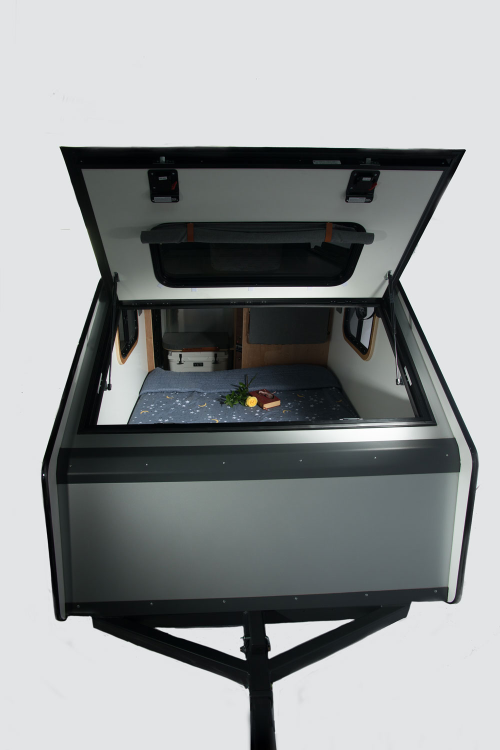 This open mini camper, ideal for RV rental, showcases a cozy bed with a starry blanket, a book, and storage. Ready for your adventure.. Campinawe Sport 2022