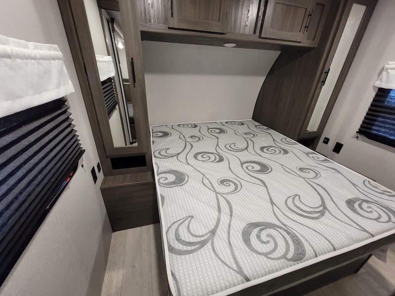 Modern RV rental bedroom: cozy bed, overhead cabinets, and built-in mirror.. Forest River Shasta 2021