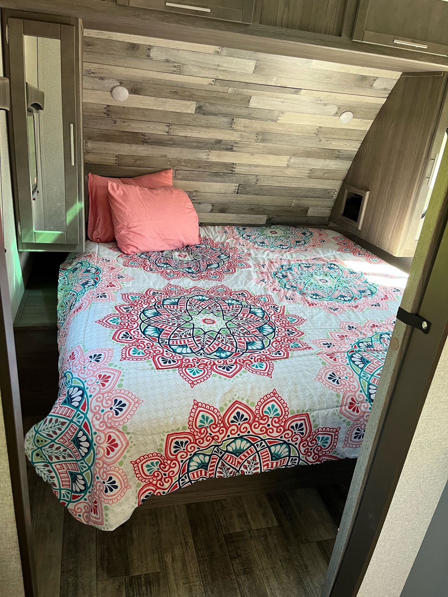 Inside an RV rental: a cozy bedroom features a vibrant mandala quilt, pink pillows, and wood-paneled walls.. Crossroads Volante 2021