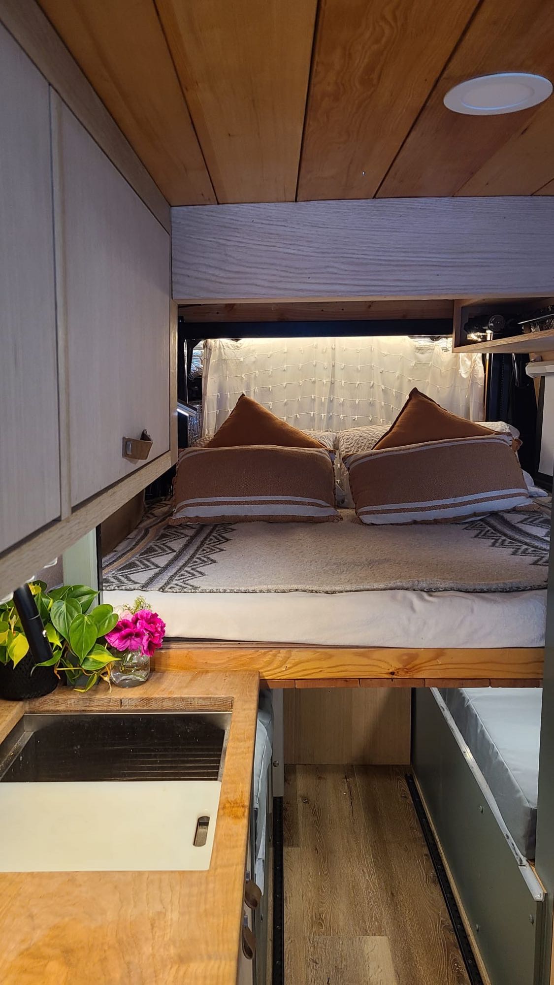 Cozy RV rental interior with wooden details, featuring a comfortable bed and compact kitchen area with a sink.. Mercedes-Benz Sprinter 2019