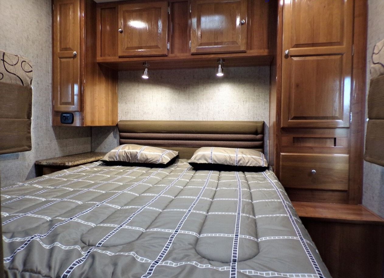 Cozy RV rental bedroom with wood cabinets, a comfy bed, and reading lights, perfect for travel.. Coachmen Leprechaun 2018