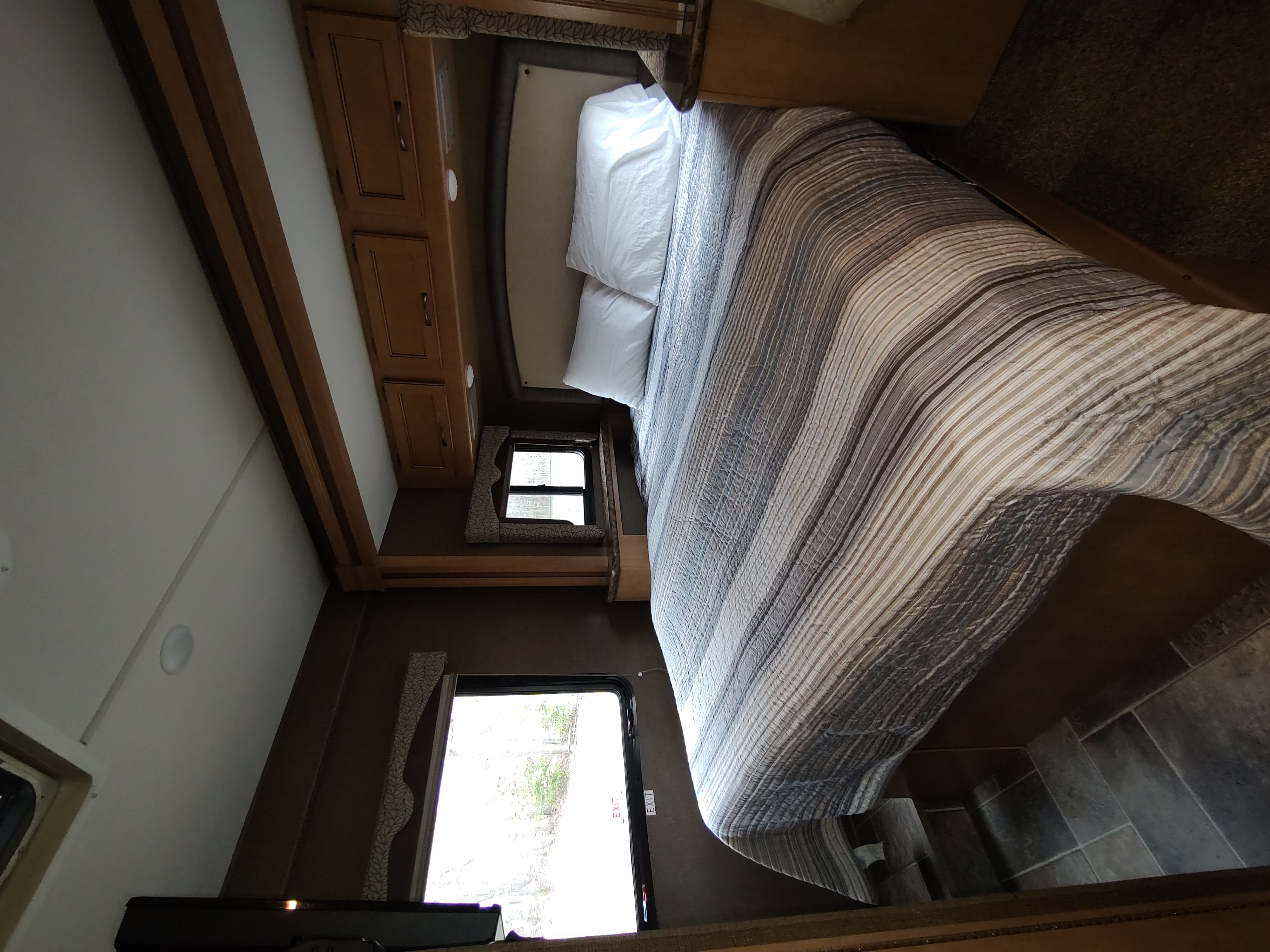 RV rental bedroom interior: a comfortable bed with striped comforter, built-in storage, and an exit door, offering a cozy retreat.. Thor Freedom Elite 2017