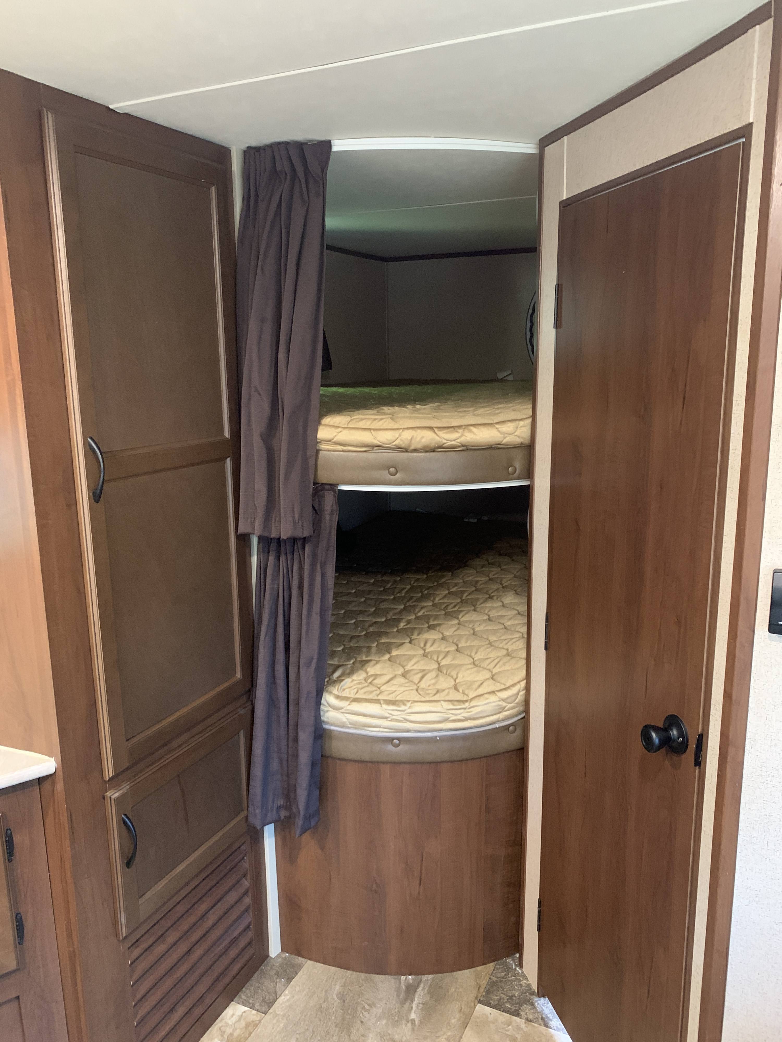 RV rental interior: cozy bunk beds with quilted mattresses & dark privacy curtains, next to a wood-paneled wardrobe.. Jayco Jay Flight 2015