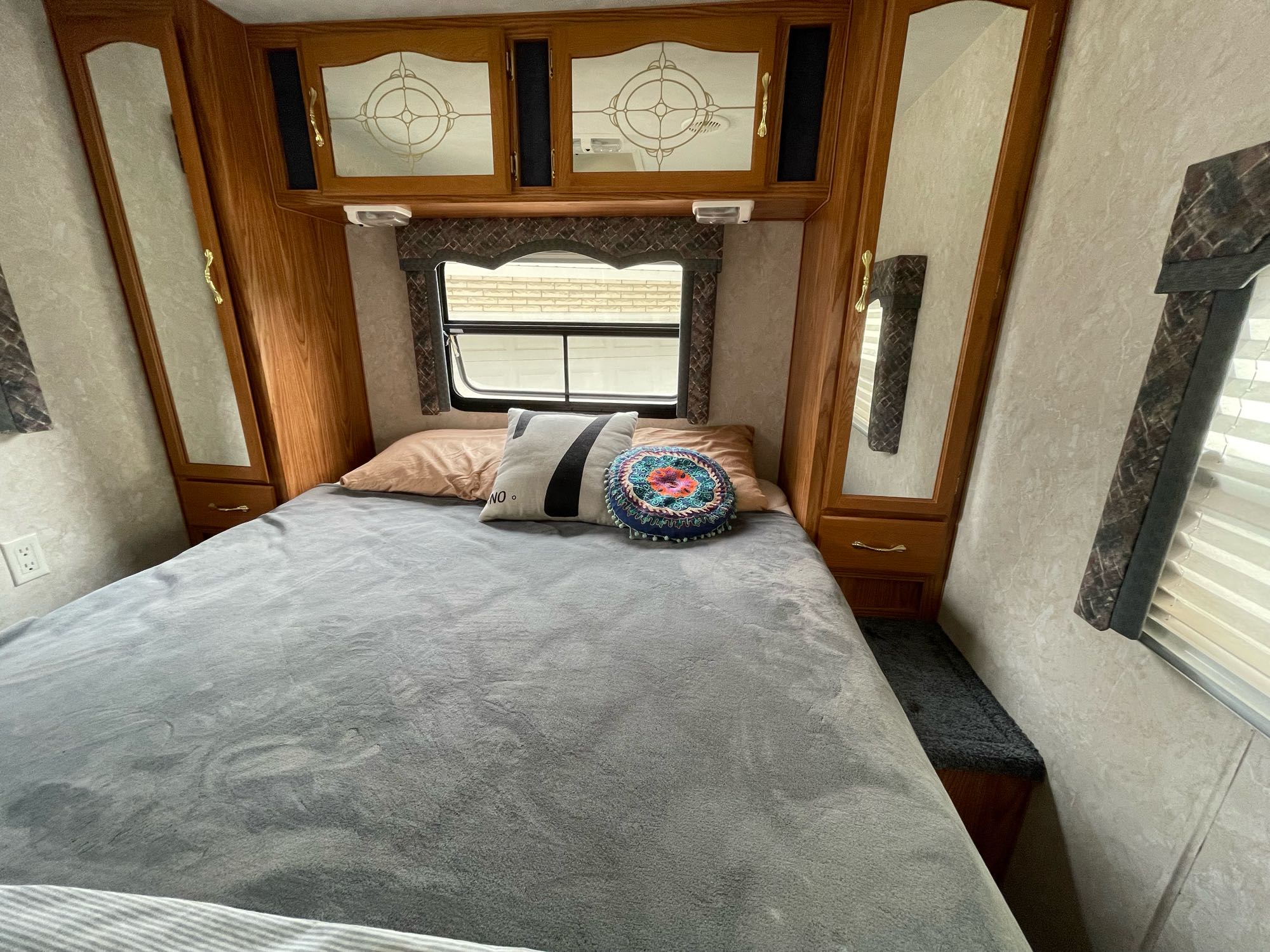 Cozy RV rental bedroom with a bed, wooden cabinets, mirrored closets, and a window for natural light.. Komfort Komfort 2003