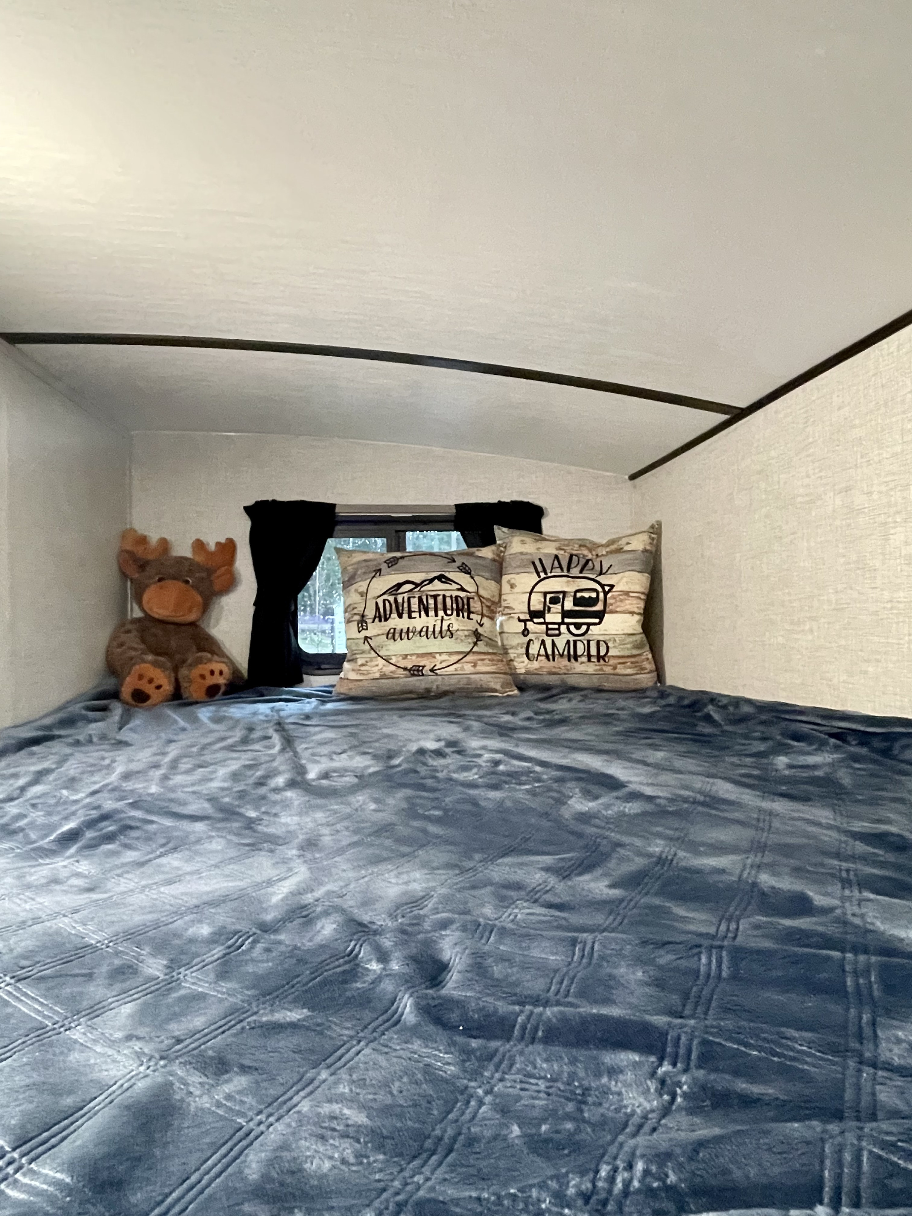 Cozy RV rental bunk bed with a blue blanket, "Adventure Awaits" and "Happy Camper" pillows, and a plush moose.. Crossroads Sunset Trails 2022