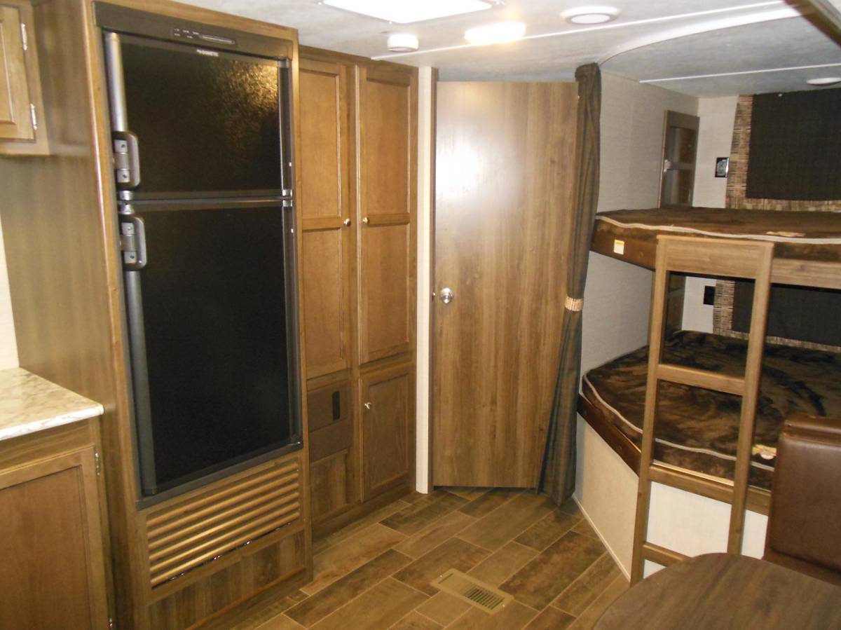 RV rental interior showcasing a large fridge, ample cabinets, and cozy bunk beds with ladder. Ideal for family travel.. Keystone RV Bullet Ultra Lite 2017