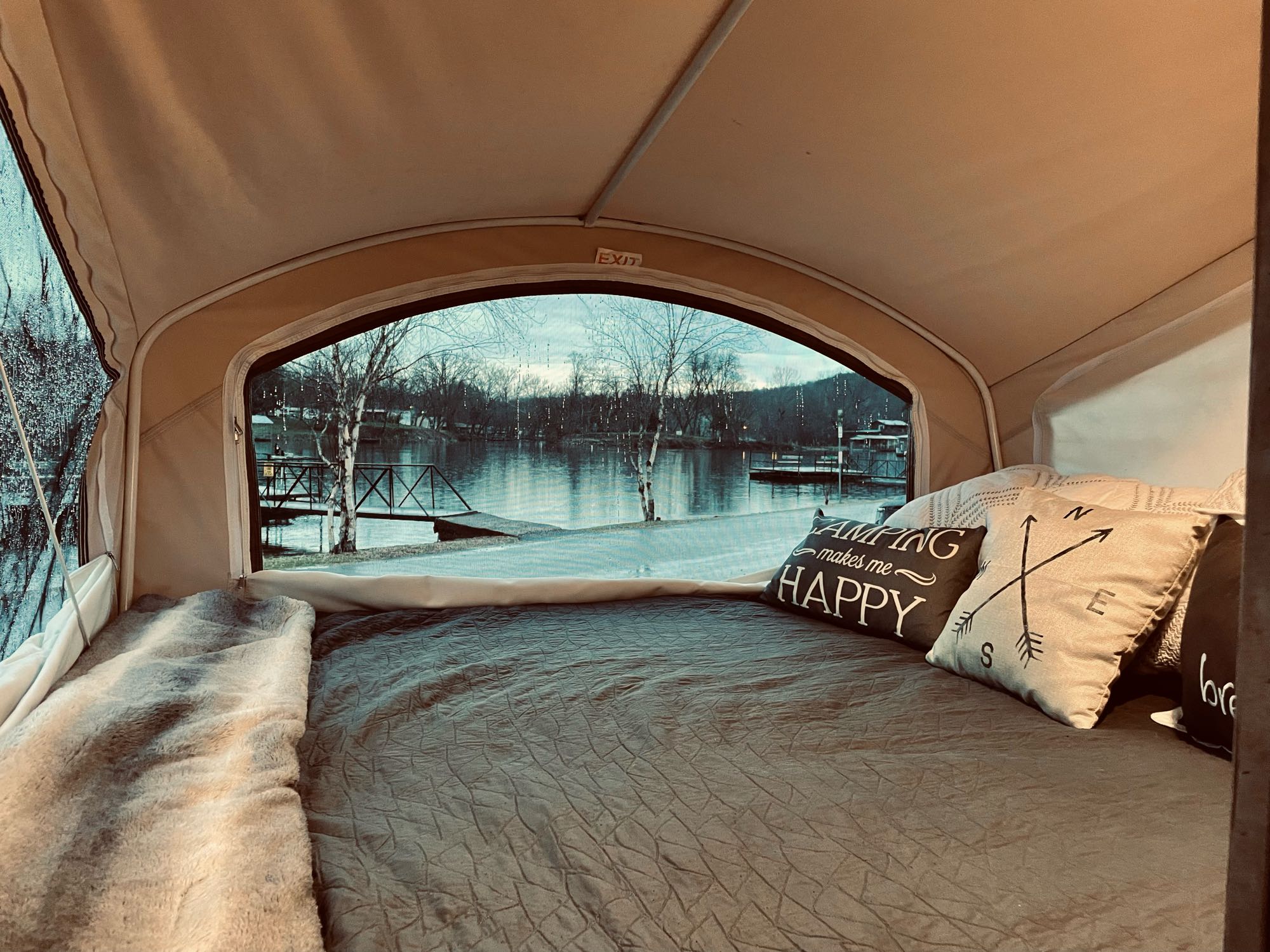 Inside a comfy RV rental: A bed with 'Camping makes me happy' pillows overlooks a calm lake. Your perfect travel retreat.. Coachmen CLIPPER 16RBD 2016