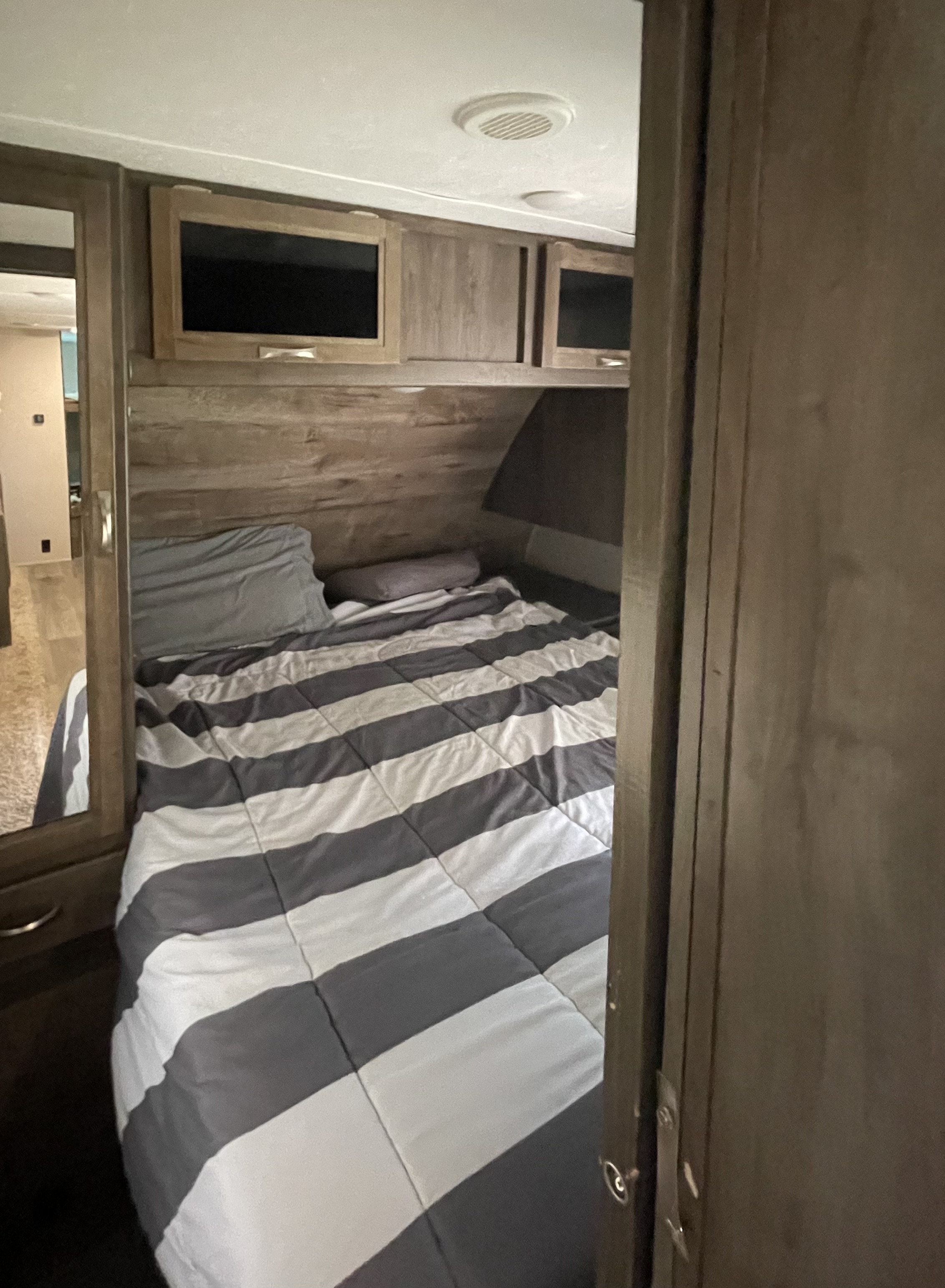 Comfortable RV rental bedroom featuring a striped bed, mounted TV, and overhead storage for your road trip comfort.. Dutchmen Coleman Light LX 2018