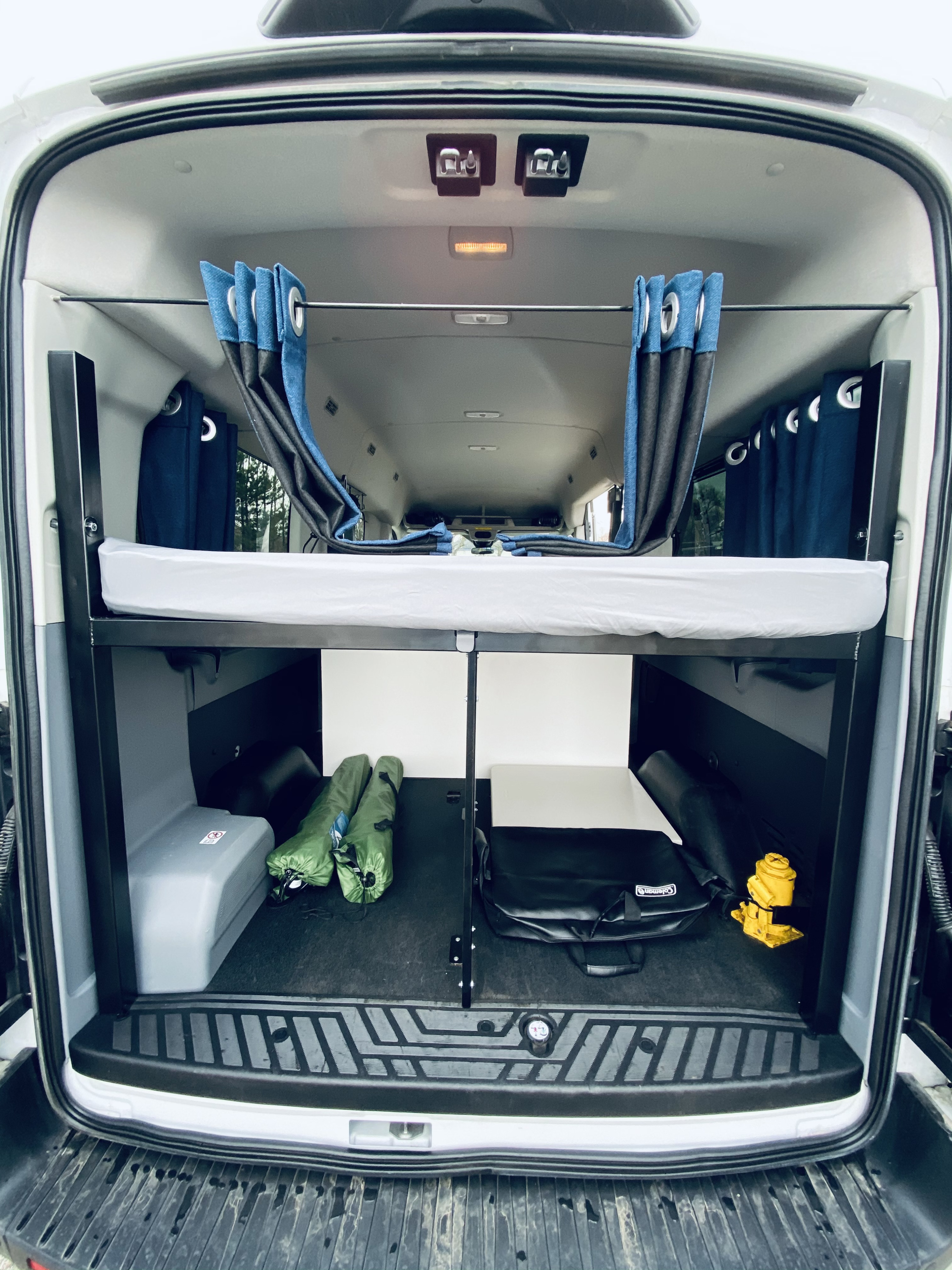 Experience RV rental comfort: a cozy bunk bed with blue privacy curtains, and smart storage below in this camper van.. Ford Transit 2017