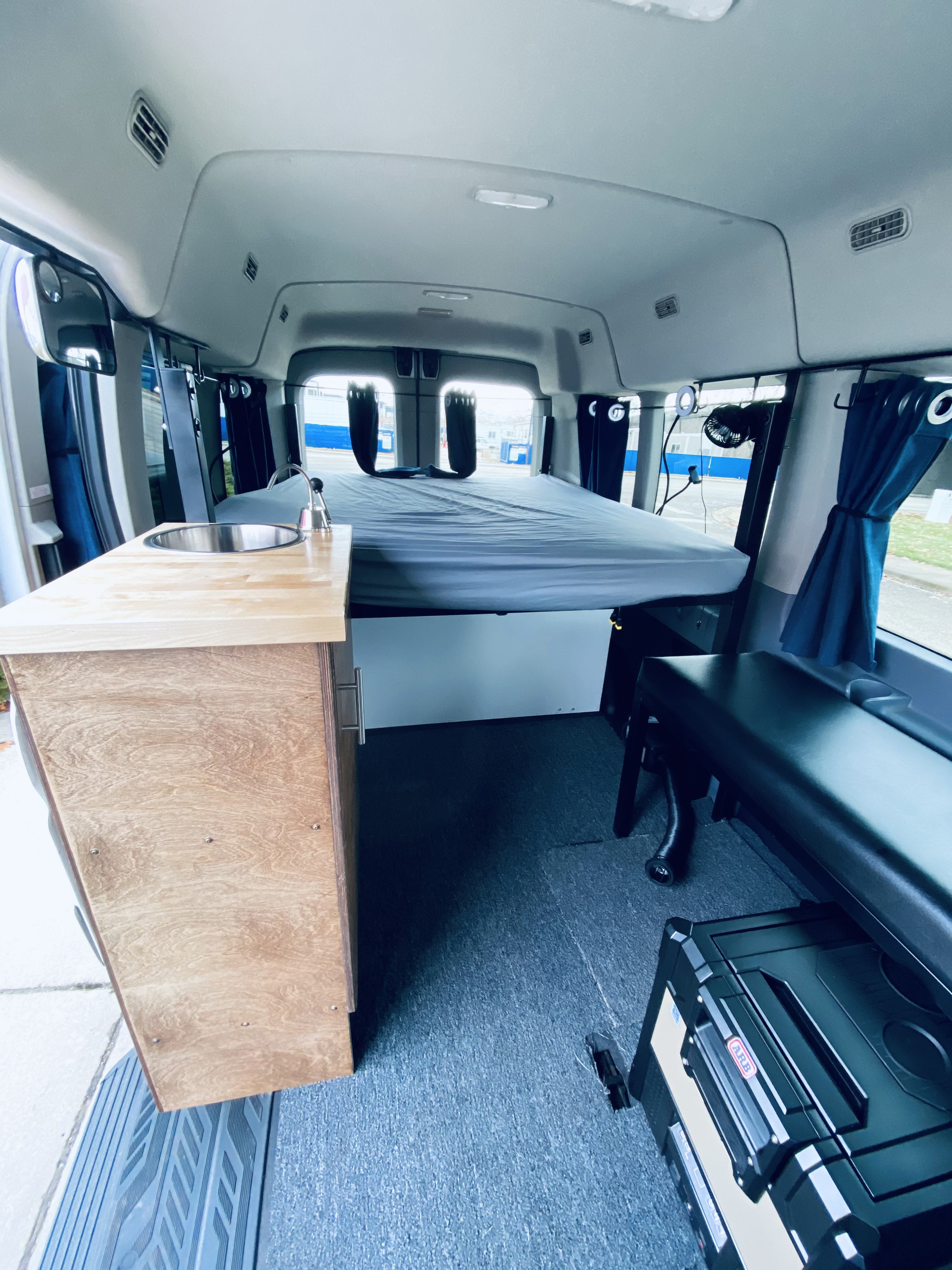 Compact RV rental interior featuring a comfy bed, functional kitchenette with sink, and efficient storage for your road trip comfort.. Ford Transit 2017
