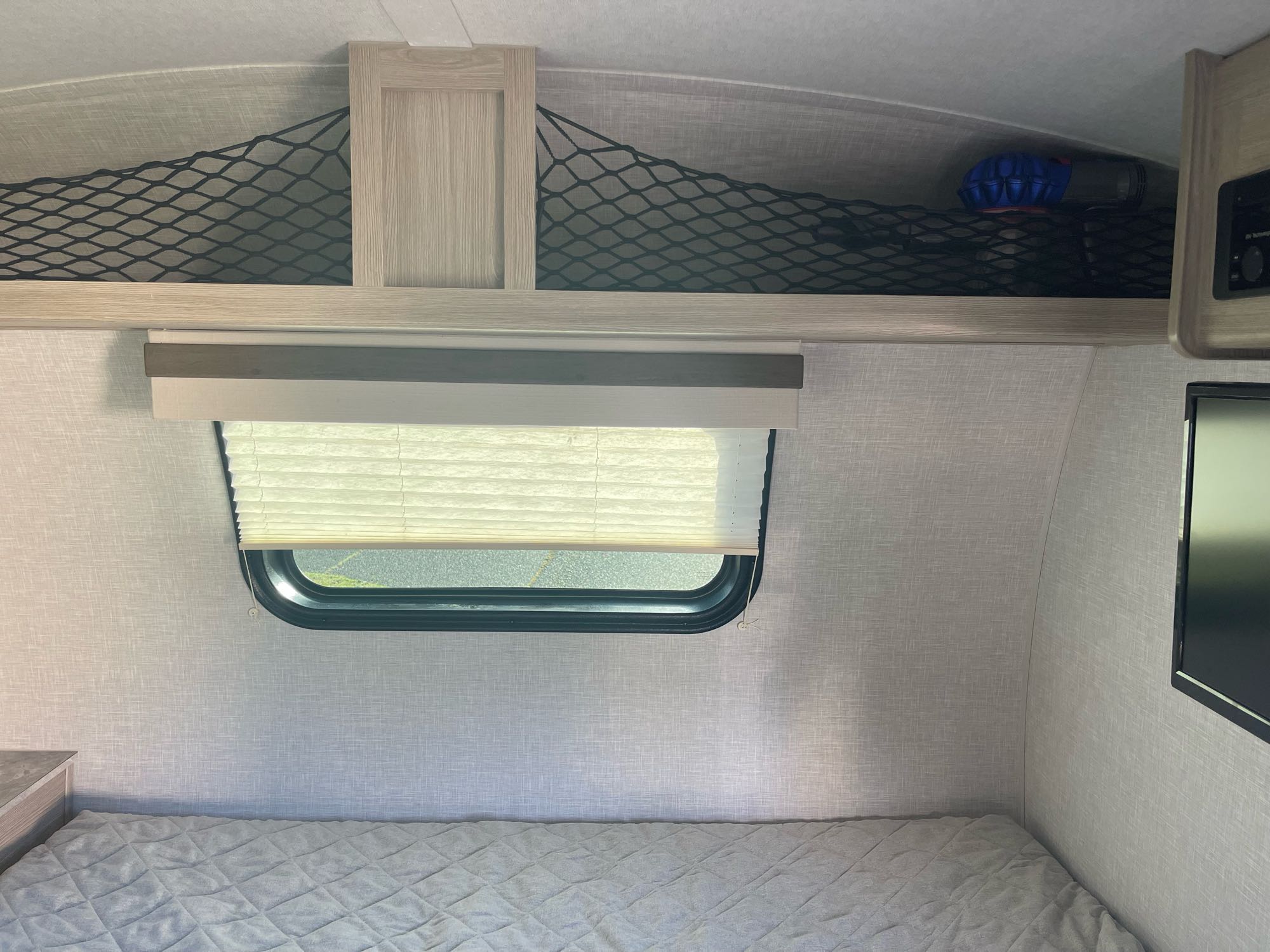 RV rental interior: light-toned bedroom with window, quilted bed, and practical overhead net storage for travel essentials.. Forest River Other 2022