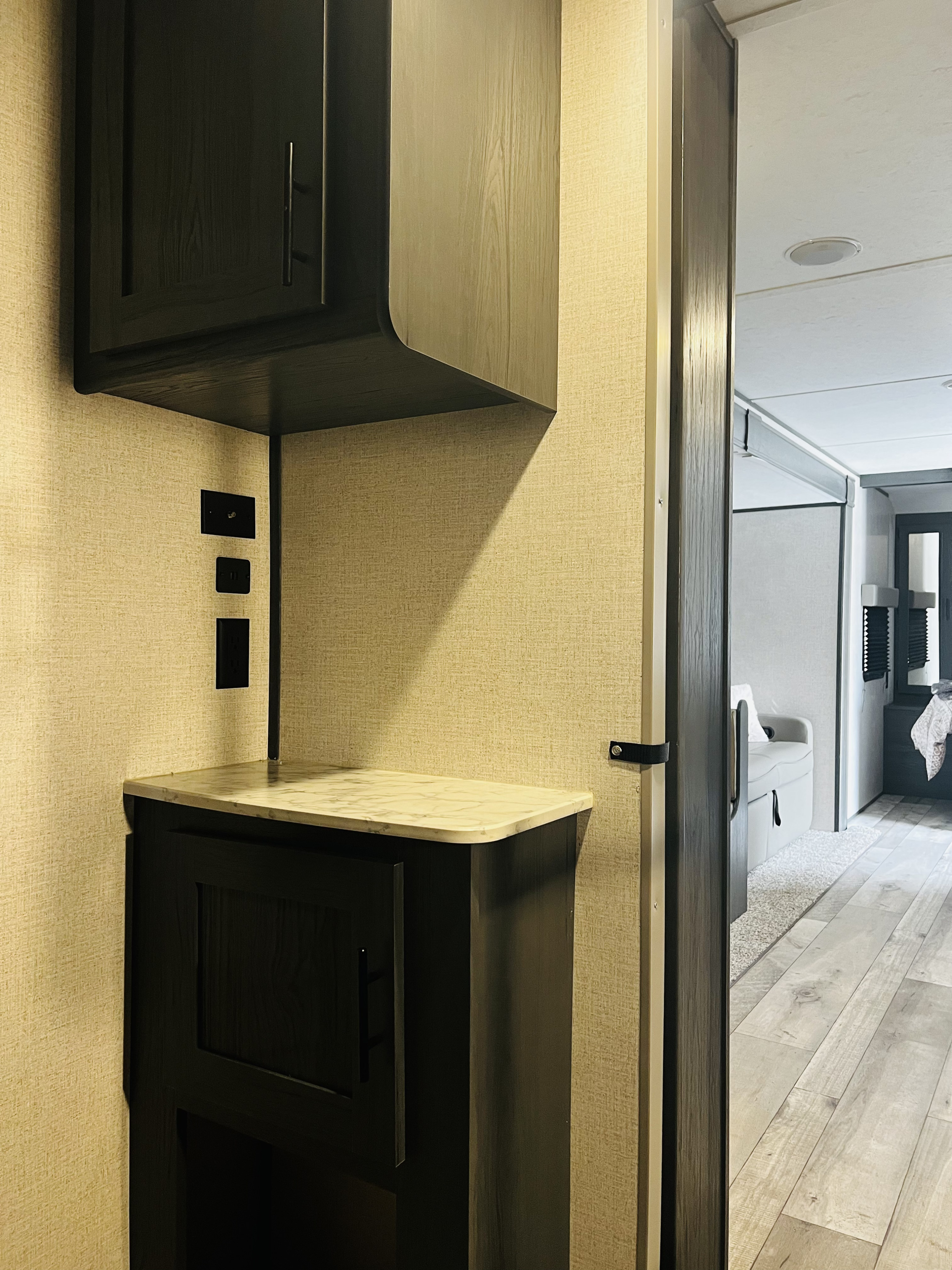 Functional RV rental interior with dark storage cabinets, marble countertop, and outlets, leading to the living space.. Dutchmen Aspen Trail LE 2023