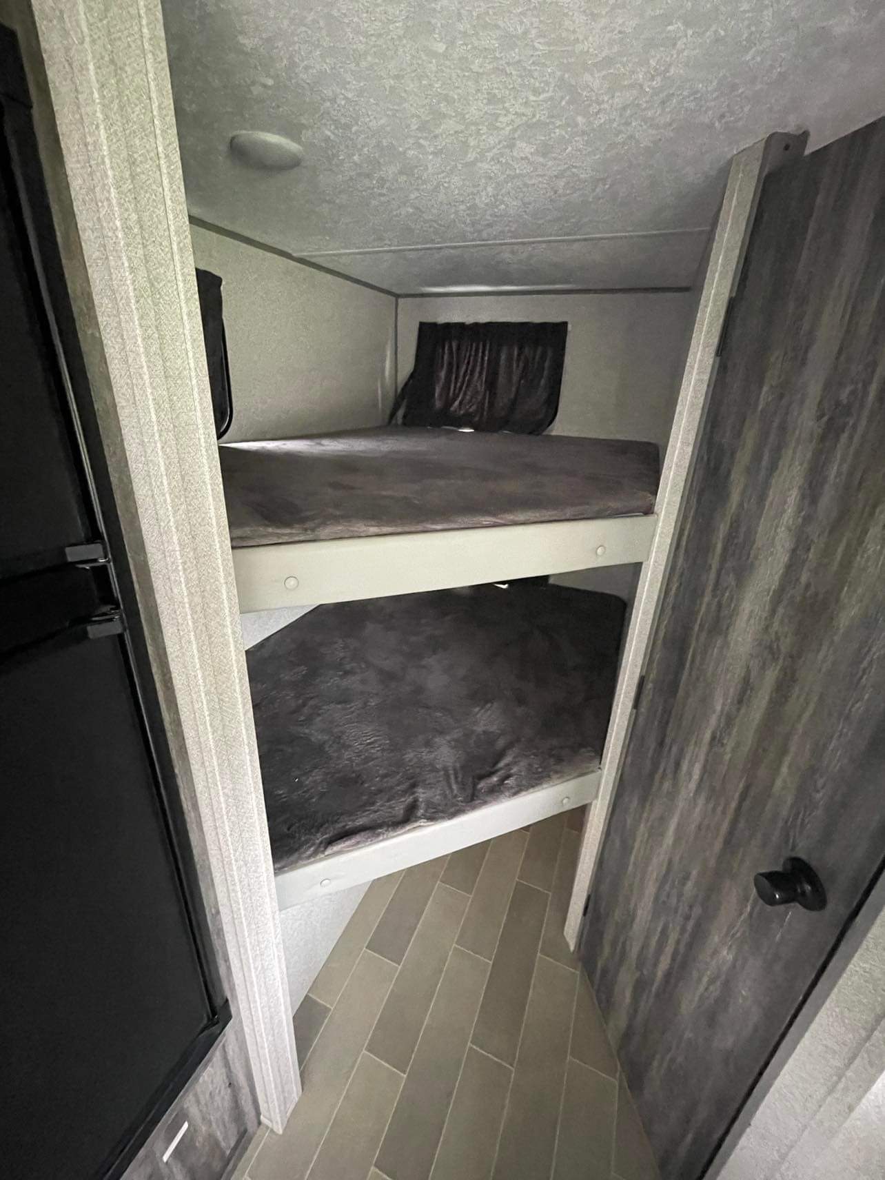 Compact RV rental bunk beds, ready for travelers. Two cozy sleeping areas with dark bedding, seen from the aisle.. Forest River Salem FSX 2020