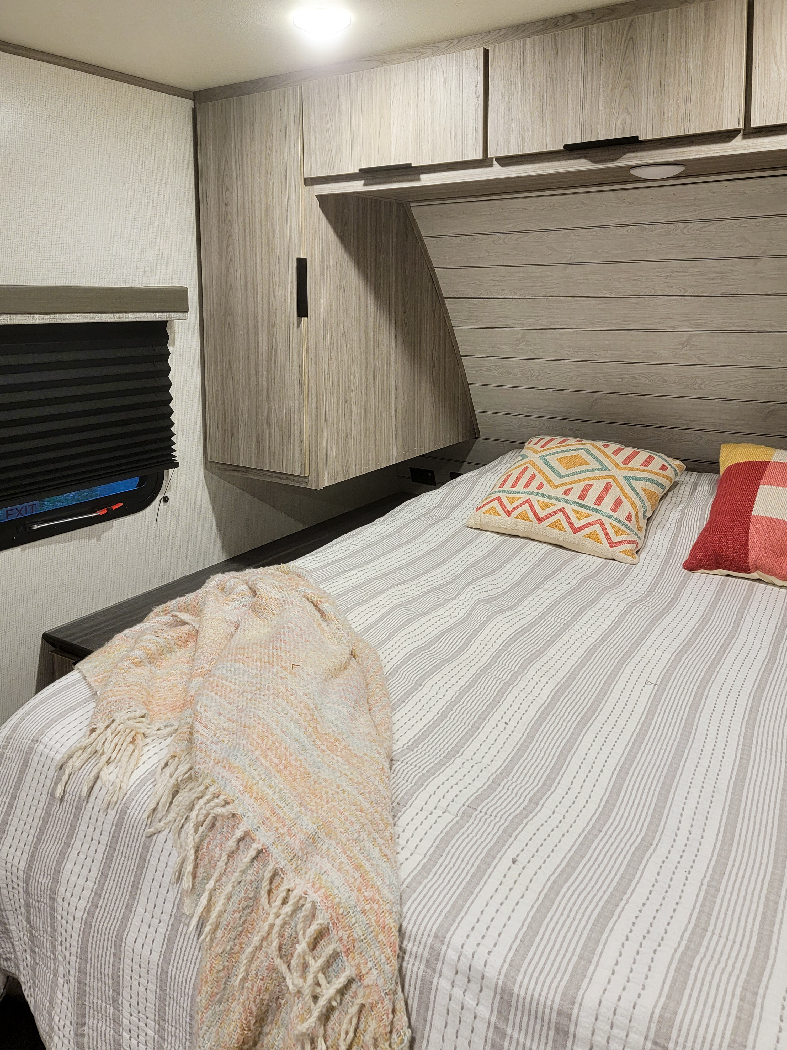 Inside a modern RV rental: a cozy bedroom with light wood cabinetry, striped bedding, and colorful pillows.. Keystone RV Passport SL 2021