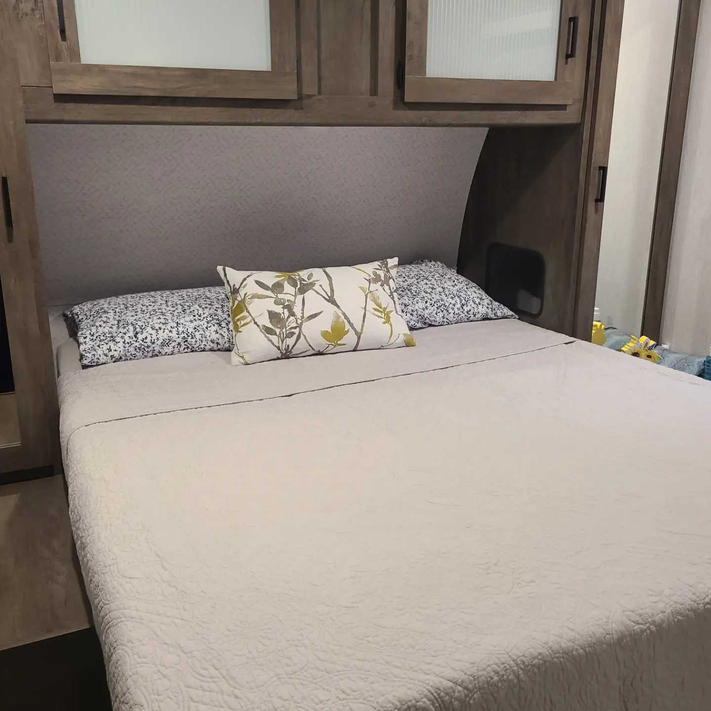 Inside an RV rental, a compact bedroom features a bed with quilted comforter, decorative pillows, and built-in wood cabinetry.. Forest River Salem 2022