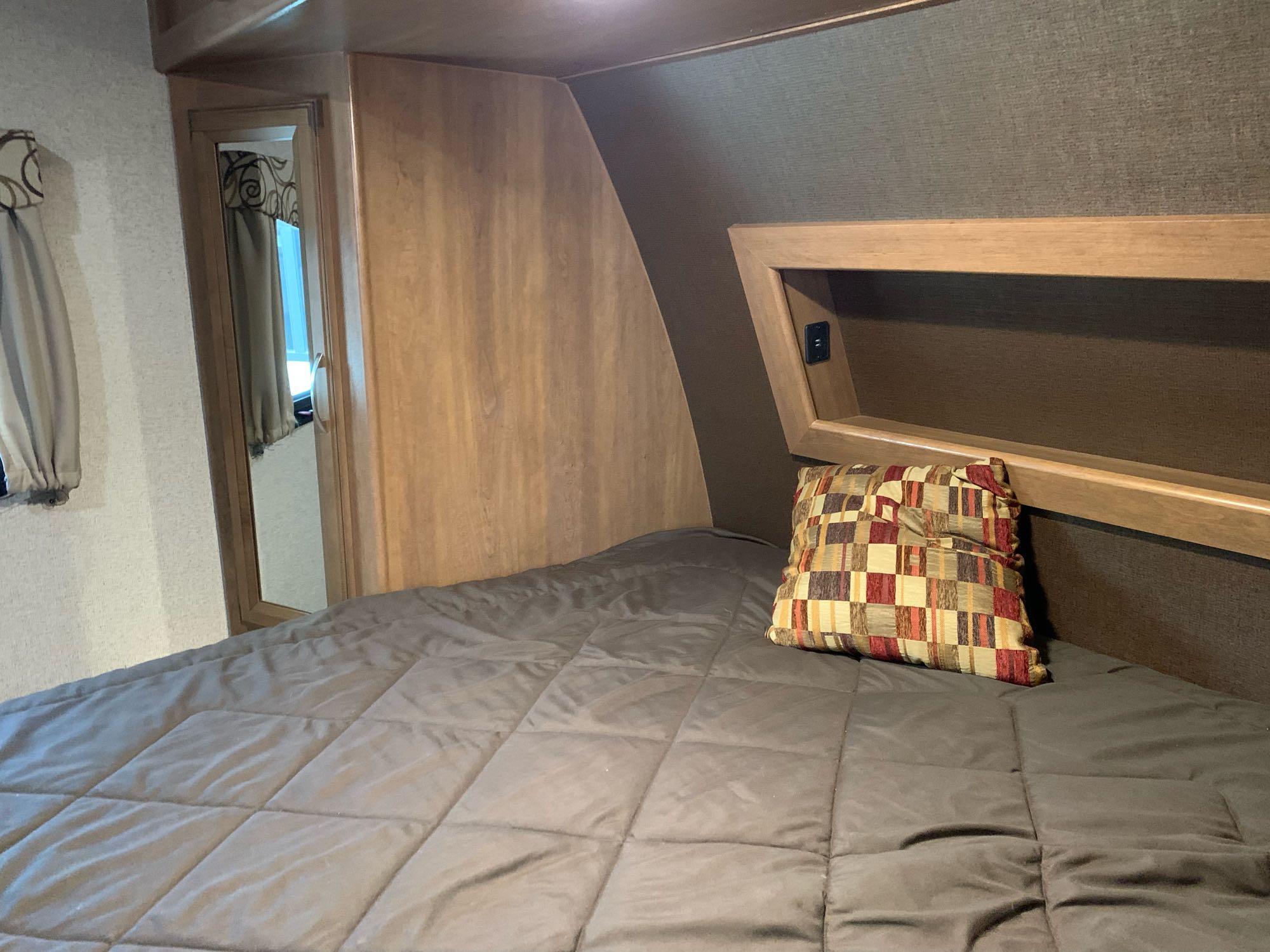 Explore this RV rental's cozy bedroom, featuring a comfy bed with integrated headboard storage and a mirrored door leading out.. Coachmen Apex 2016
