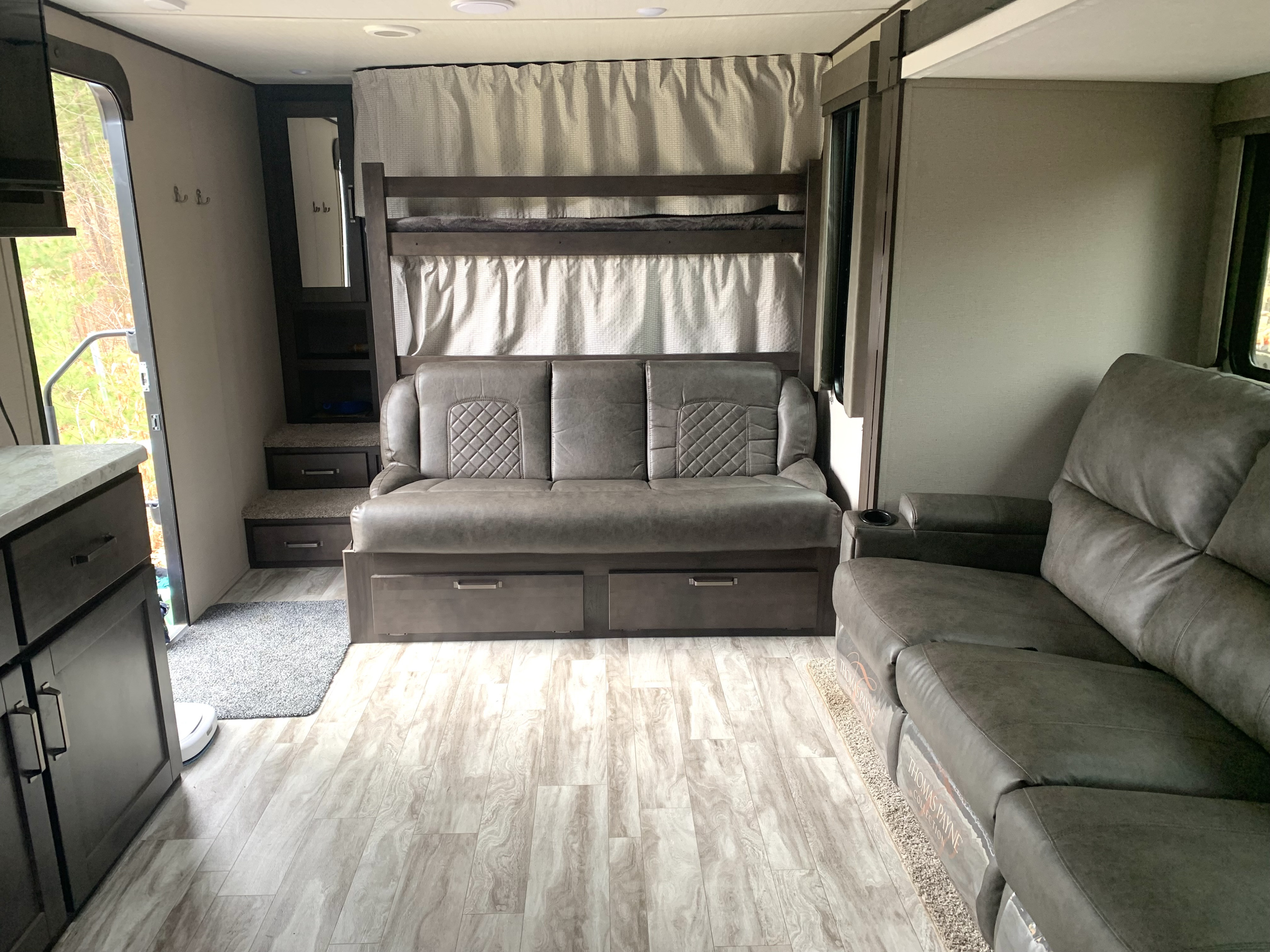 Modern rv rental interior featuring a spacious living area with sofas, convertible bunk beds, and wood-style flooring.. Grand Design Transcend Xplor 2021