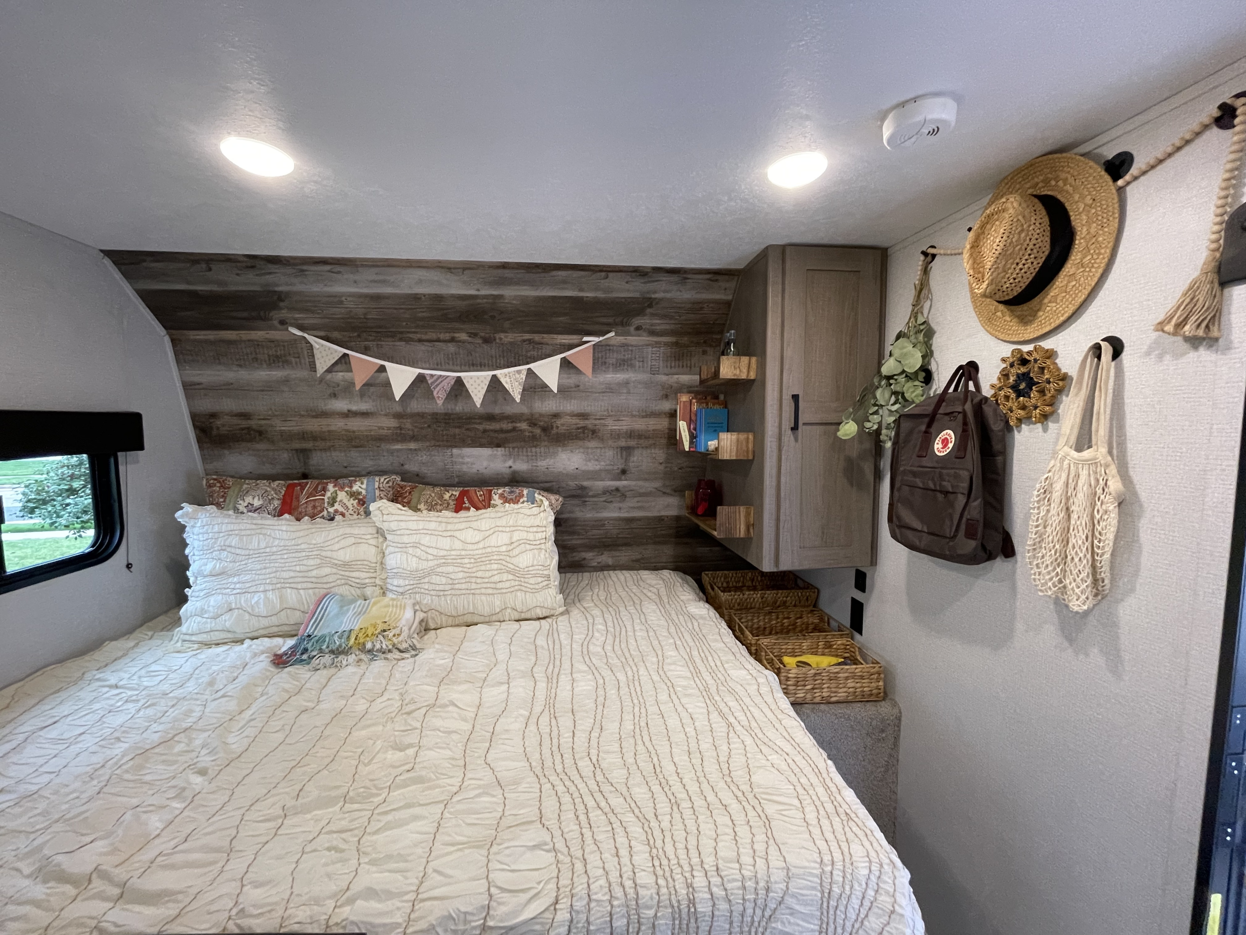 Cozy RV rental bedroom with decorated wood accent wall, comfy bed, shelves, and organized storage for travel essentials.. Keystone RV Hideout LHS Mini 2021