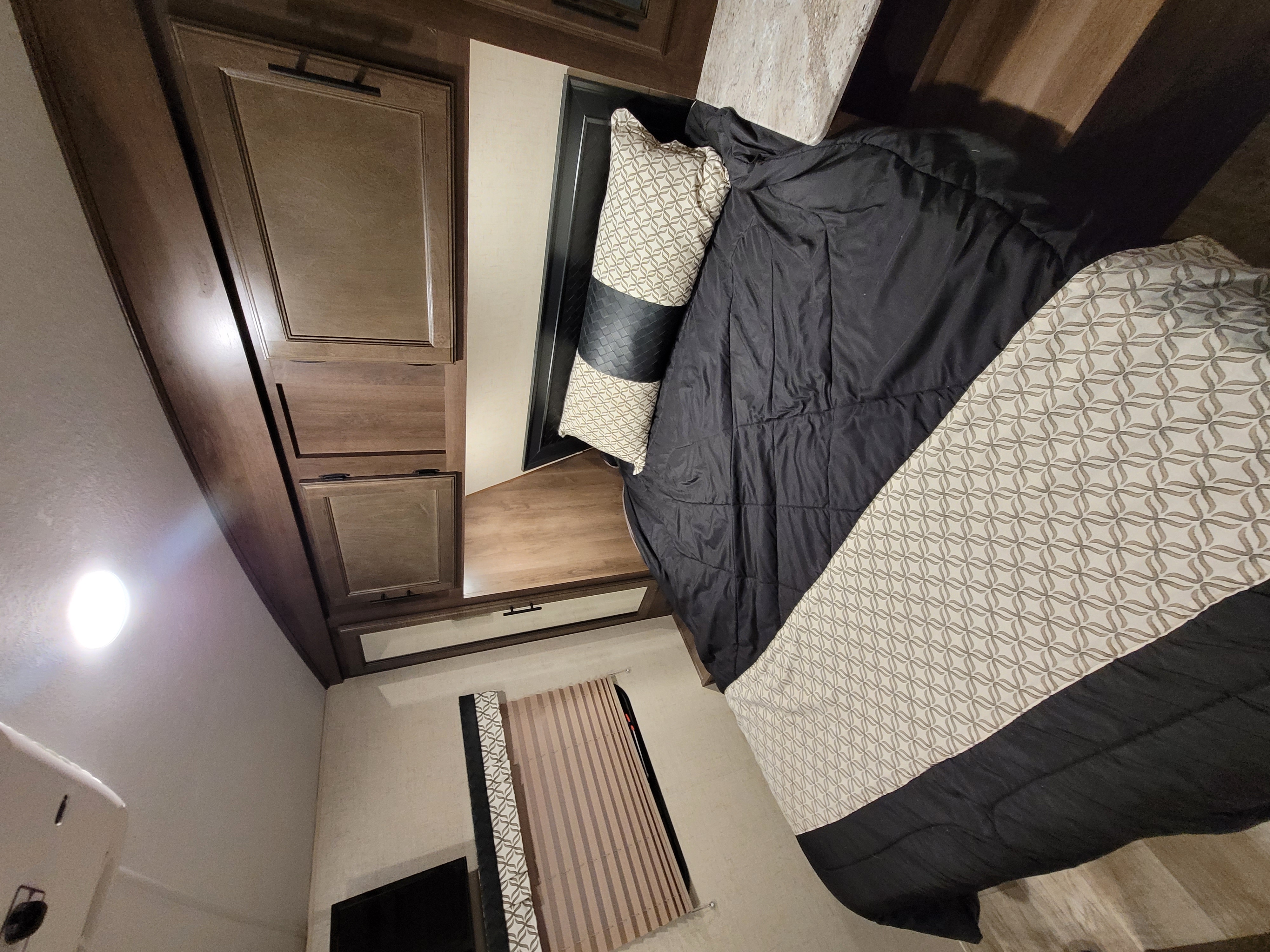 RV rental bedroom with comfortable bed, patterned bedding, wooden cabinets, and ceiling light.. Spree Spree Trailer 2018
