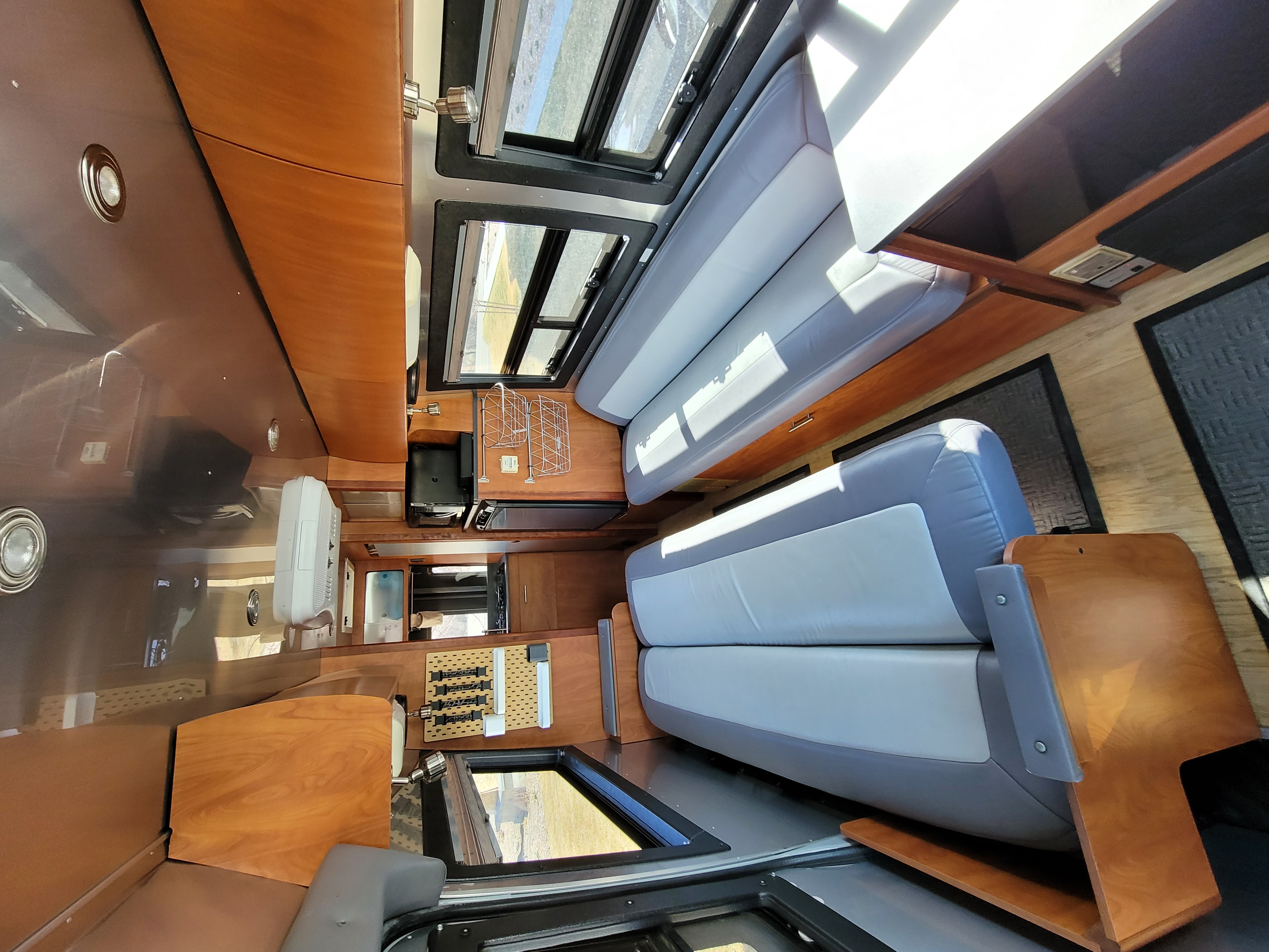 An inviting RV rental interior features plush gray seating, multiple windows, and smart storage within a warm wooden design.. Dodge Airstream Interstate Sprinter 2004