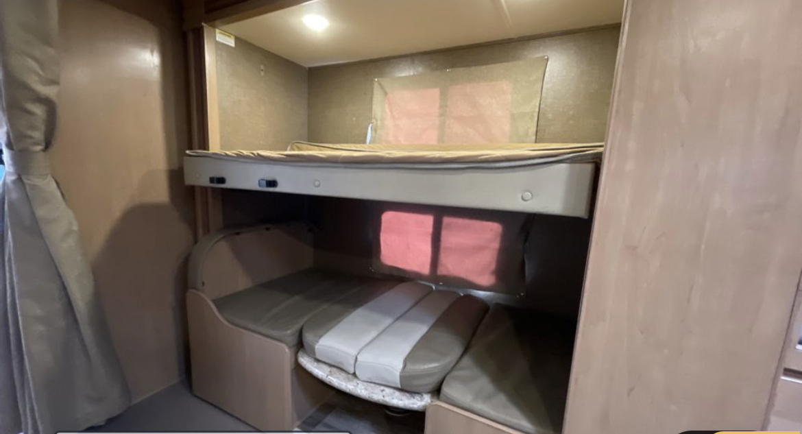 Cozy RV rental interior: bunk beds, a lower convertible sofa bed, & window shades.. Thor Motor Coach Four Winds 2020