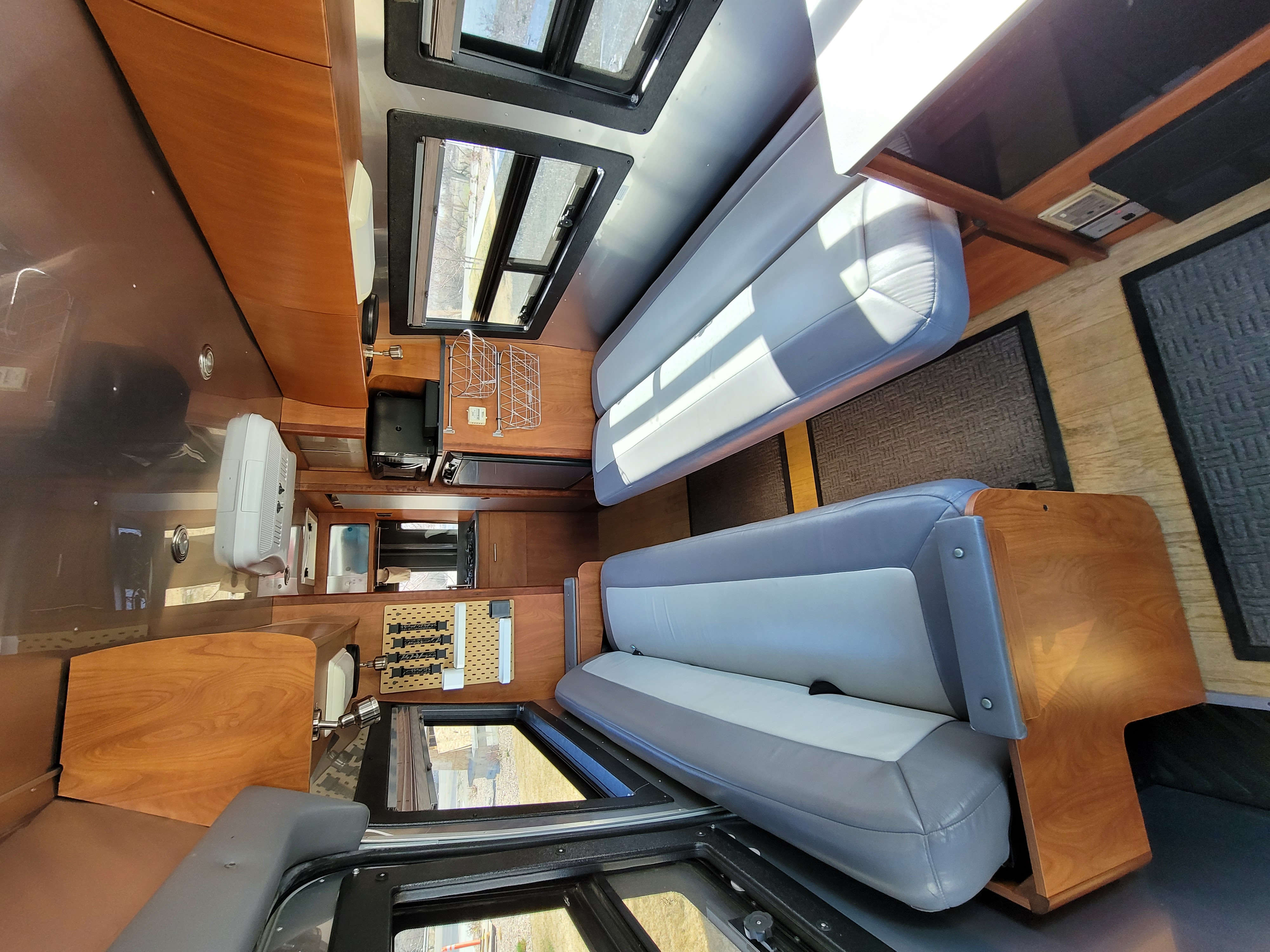 Inside an RV rental, a well-appointed interior features two seating areas, wood cabinetry, bright windows, and a compact kitchen.. Dodge Airstream Interstate Sprinter 2004