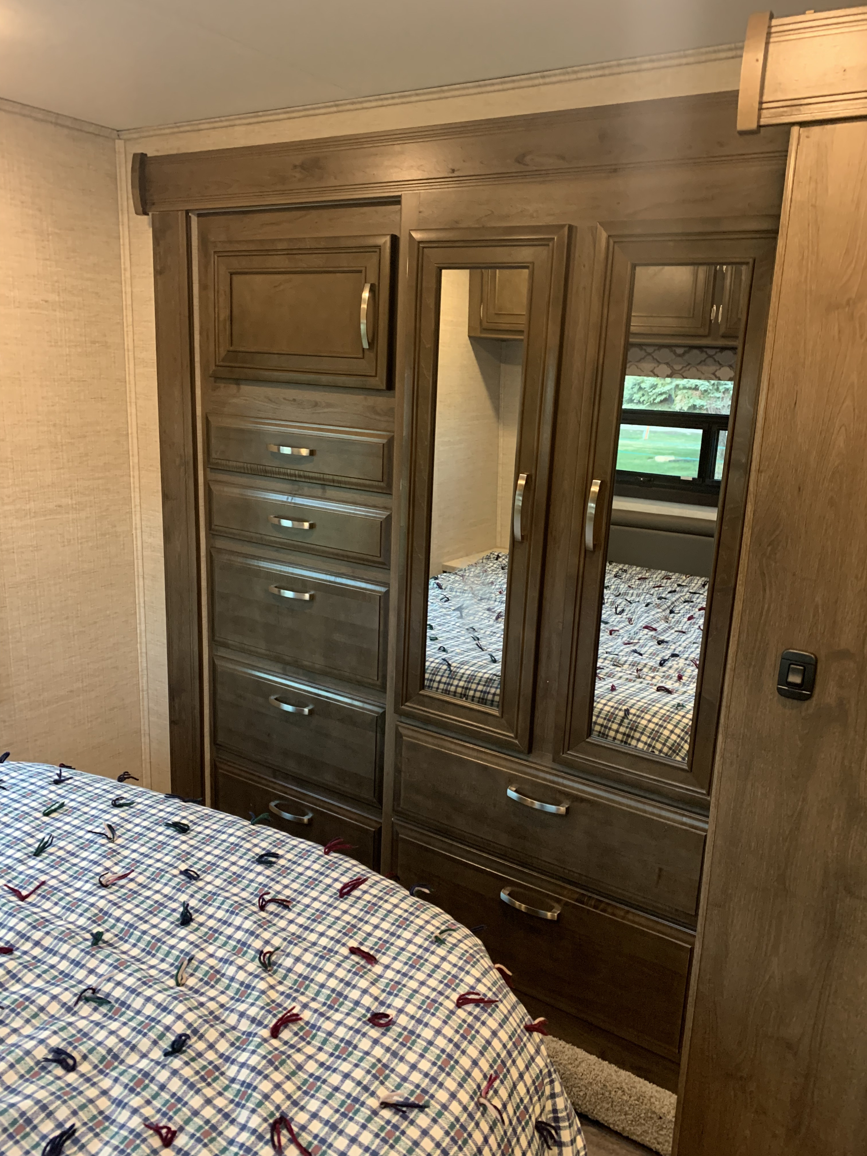 Spacious RV rental bedroom featuring a wooden mirrored wardrobe, dresser drawers, and a cozy plaid bed for comfort and storage.. Jayco Redhawk 2021