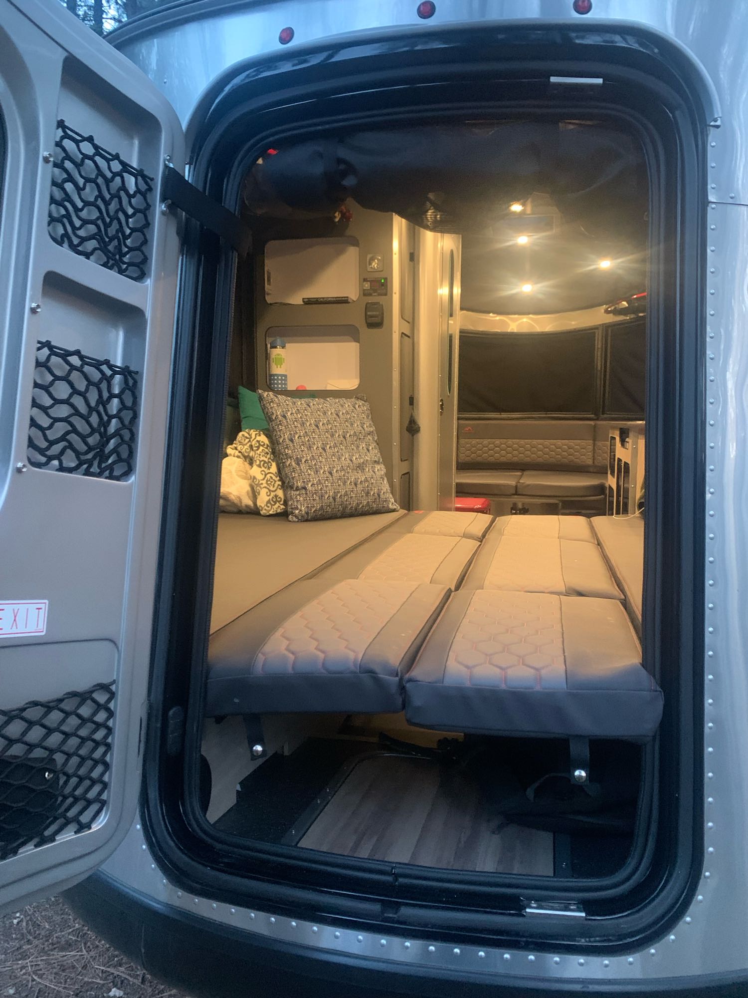 Cozy RV rental interior: foldable bed & lounge area with warm lighting, seen from the open rear door.. Airstream Basecamp 20X 2022