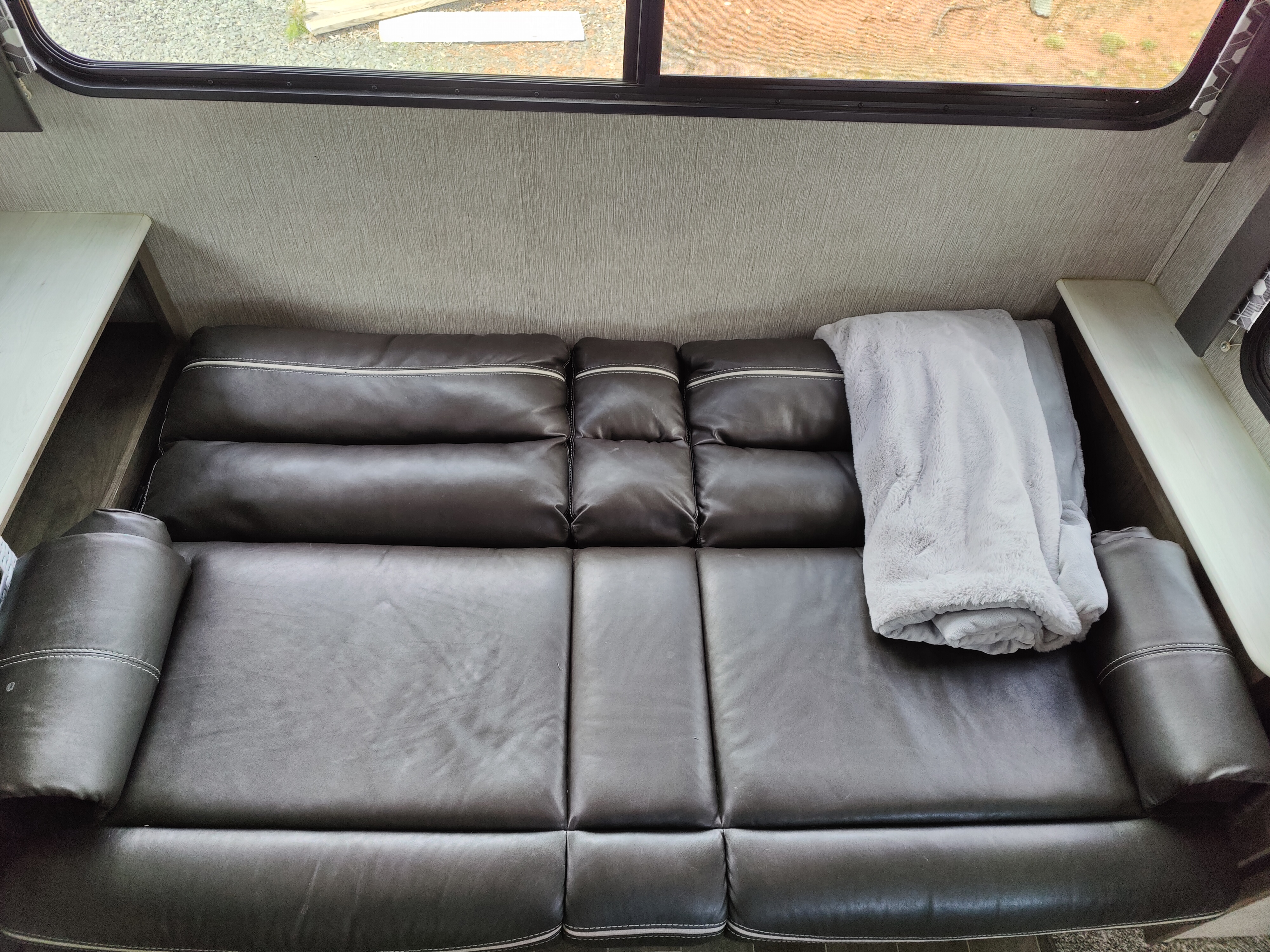 Cozy RV rental living space featuring a dark leather sofa, soft blanket, and natural light from windows.. Dutchmen Coleman Light 2020