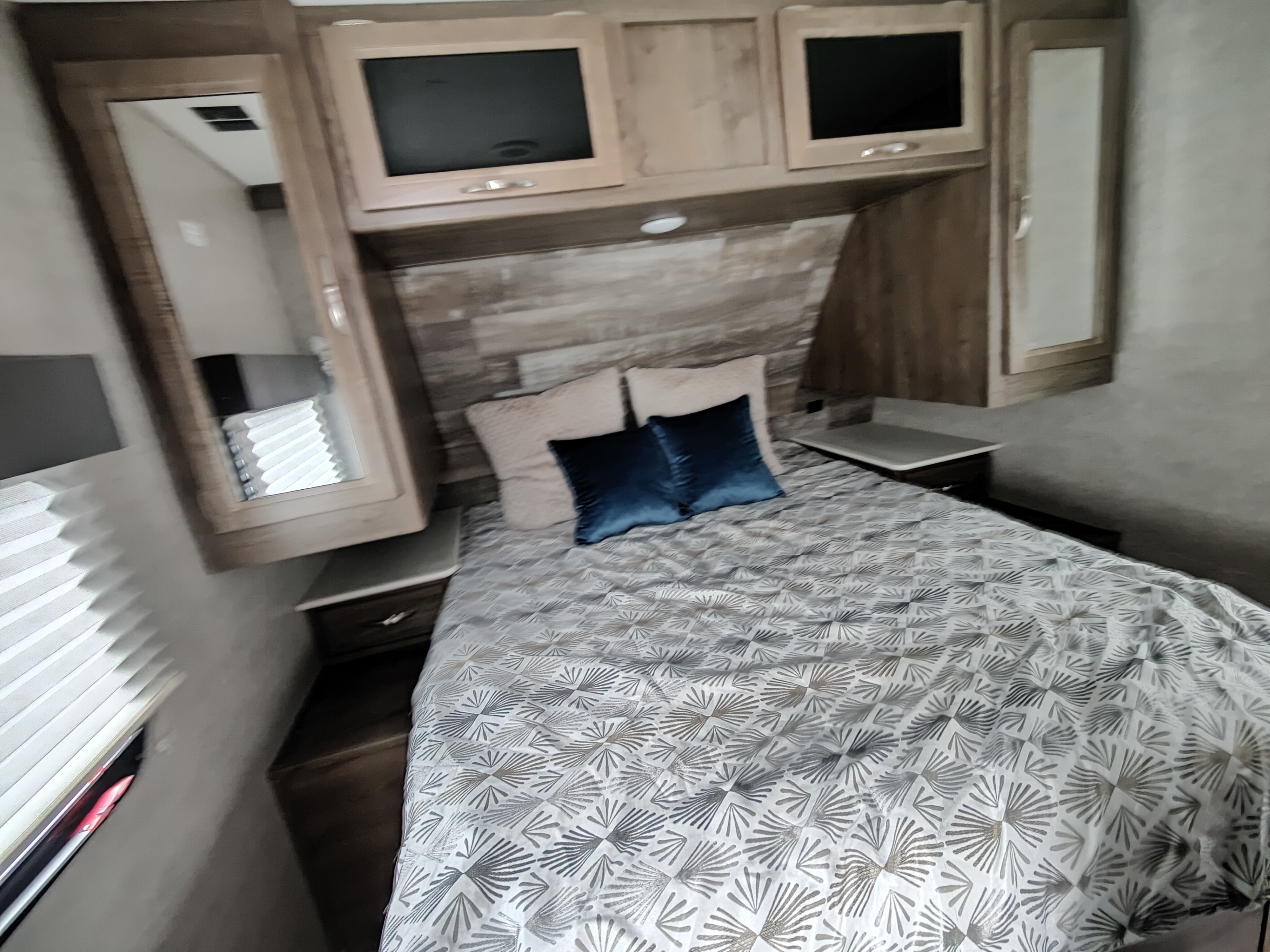 This RV rental features a cozy bedroom with a patterned bed, blue pillows, and integrated TVs/storage cabinets.. Dutchmen Coleman Light 2020