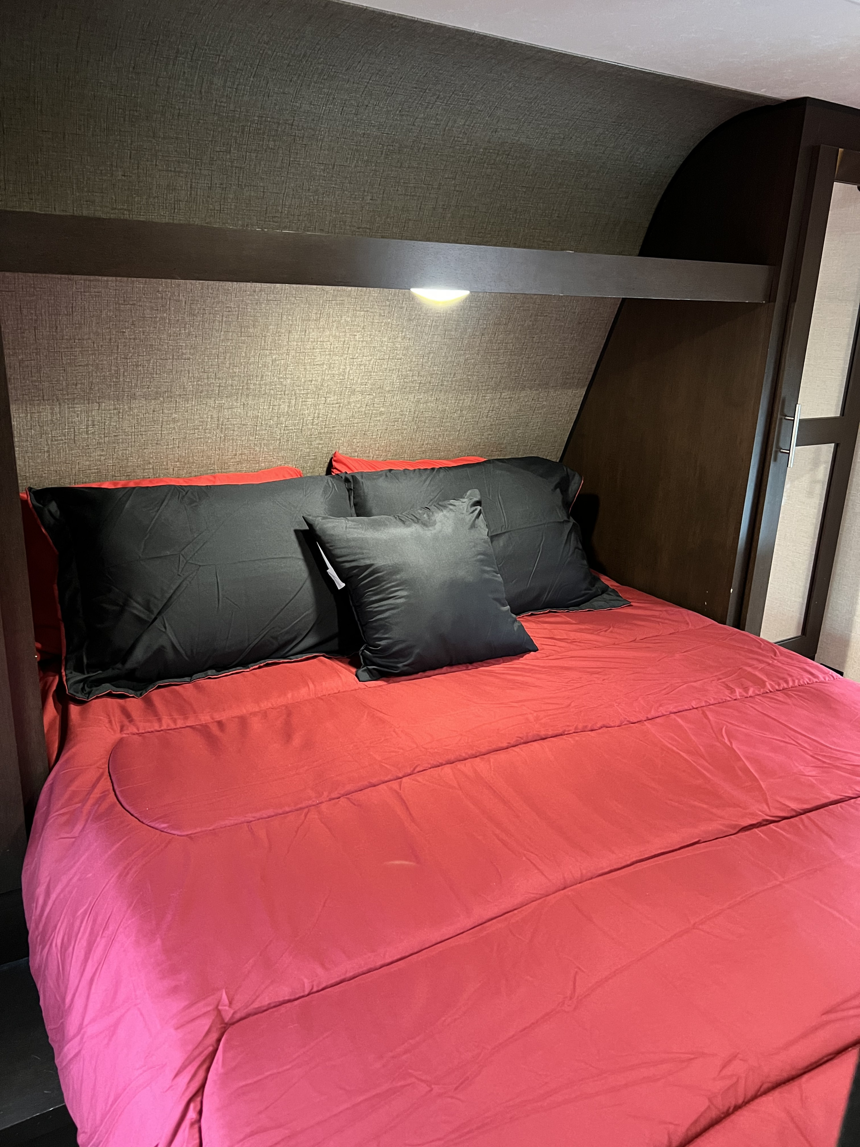 Inviting RV rental bedroom: red comforter, black pillows, and a built-in reading light. Perfect for travel.. KZ Sportsmen 2018