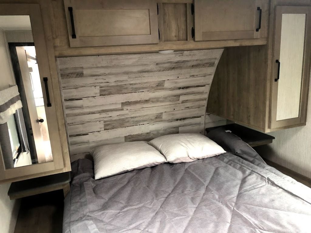 RV rental bedroom with bed, stylish wood paneled headboard, overhead cabinets, and mirrored closet.. Palomino Puma Unleashed 2021