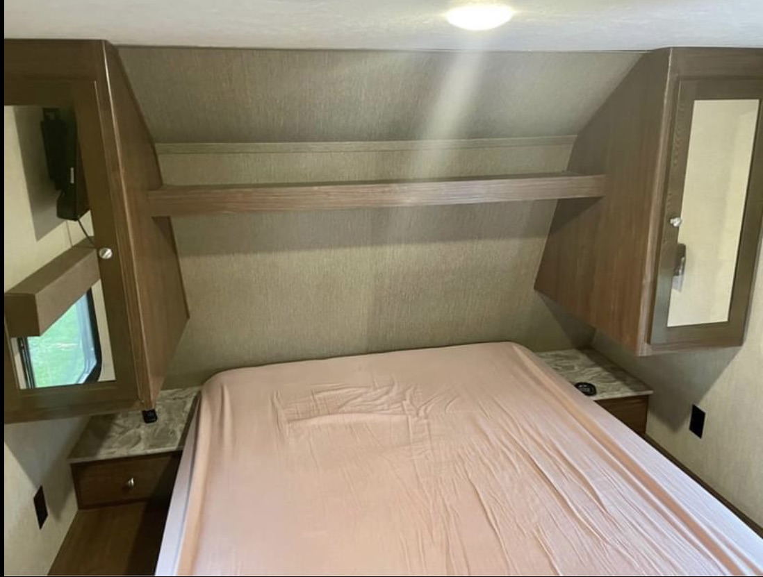 Cozy RV bedroom with bed, overhead storage, and nightstands. Perfect for your next rv rental adventure.. Dutchmen Coleman Lantern Toy Hauler 2018