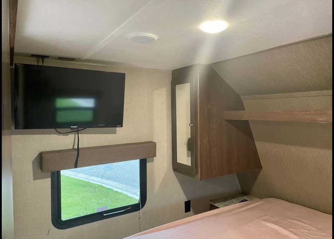 RV rental bedroom with wall-mounted TV, window, bed, and built-in storage. Perfect for road trips.. Dutchmen Coleman Lantern Toy Hauler 2018