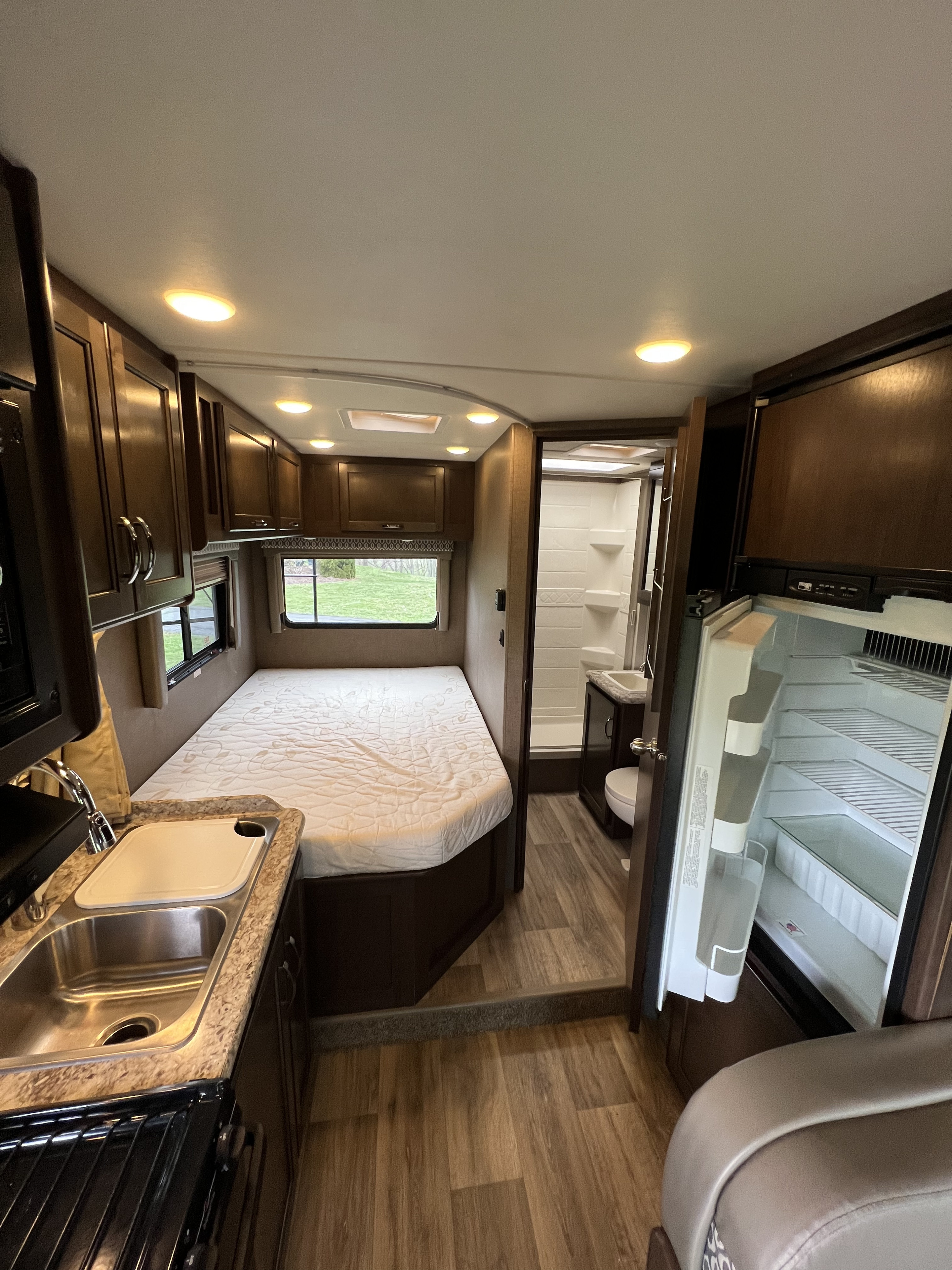 Inside a modern RV rental: a compact kitchen, comfortable bed, full bathroom, and refrigerator, ideal for road trips.. Thor Freedom Elite 2017