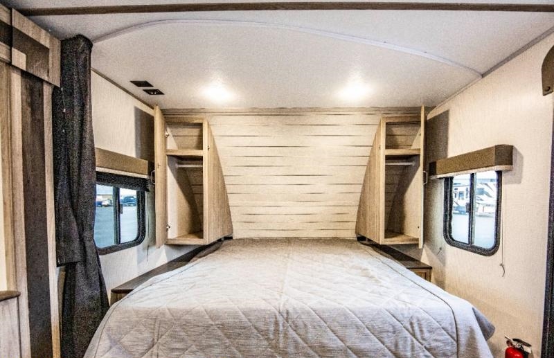 Explore this RV rental bedroom: a comfortable bed, integrated storage cabinets, and side windows, ready for your next adventure.. Keystone RV Passport SL 2021