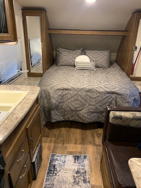 Cozy RV rental bedroom with patterned gray bedding, adjacent to a compact kitchen counter and dinette. Functional interior.. Forest River Wildwood X-Lite 2017