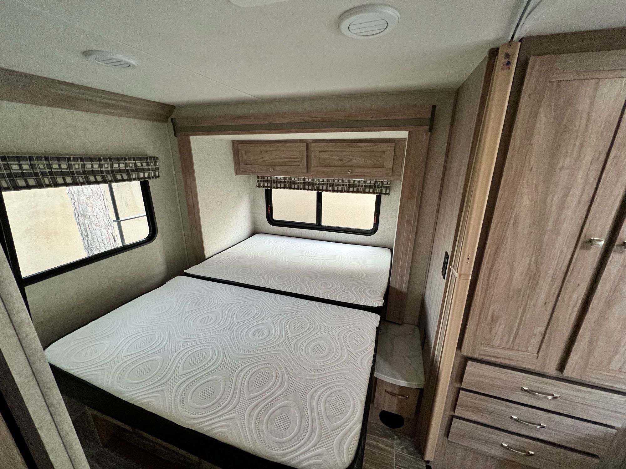 Inside an RV rental: a modern bedroom featuring two bunk beds, windows with valances, and wooden storage cabinets.. Forest River Sunseeker 2019