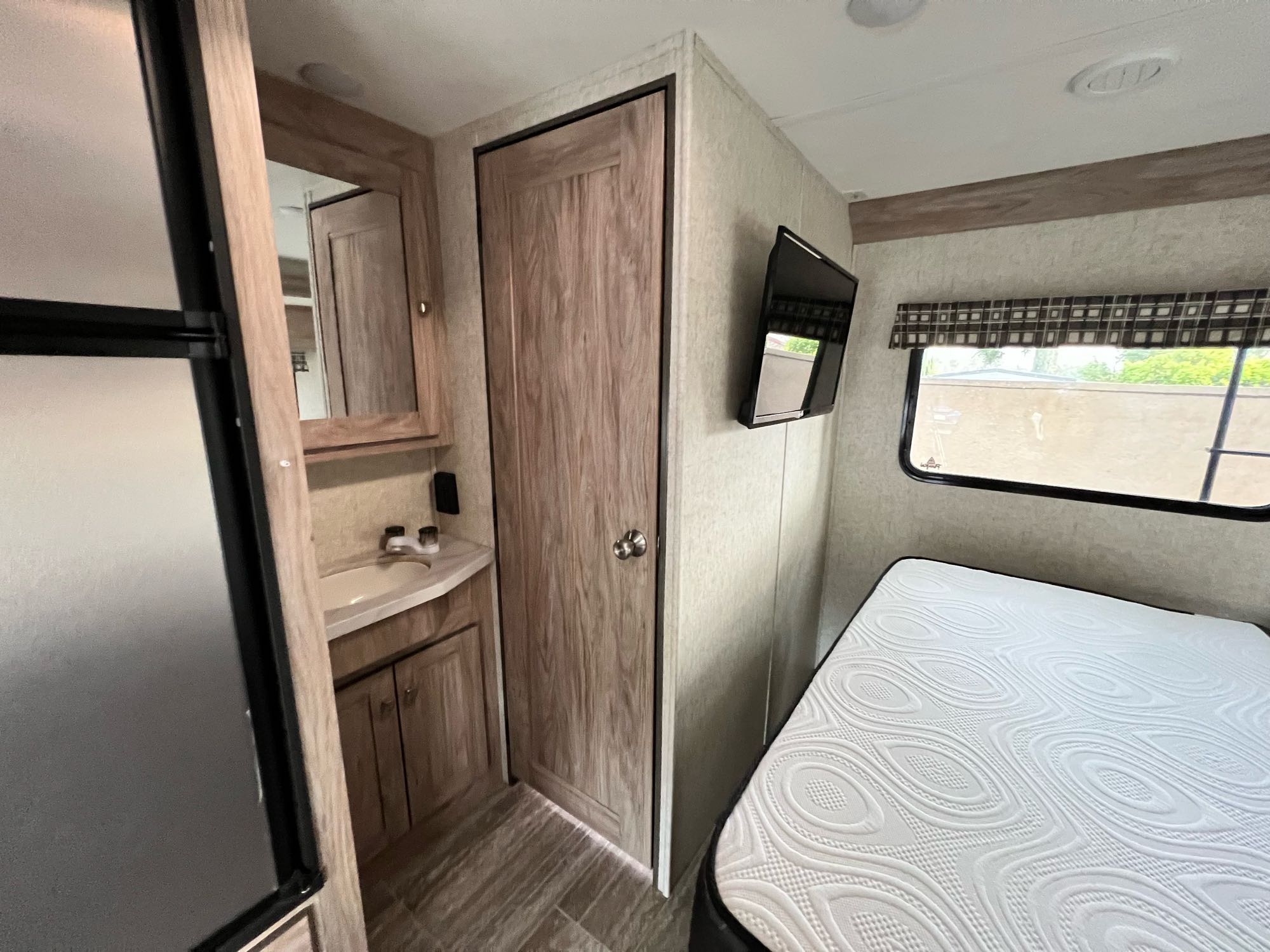 Compact RV rental interior featuring a bedroom with a clean mattress, mounted TV, and a functional bathroom vanity area.. Forest River Sunseeker 2019