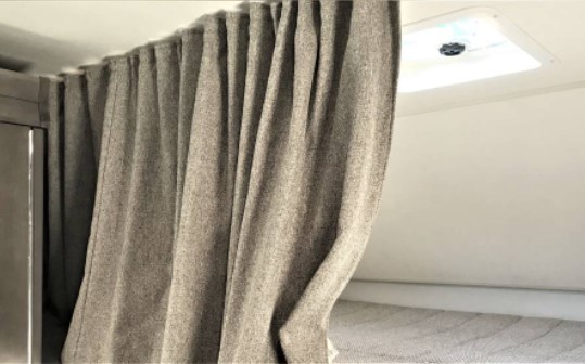 An RV rental's gray privacy curtain hangs beside a sleeping bunk, with a white ceiling vent visible.. Winnebago Minnie Winnie 2020