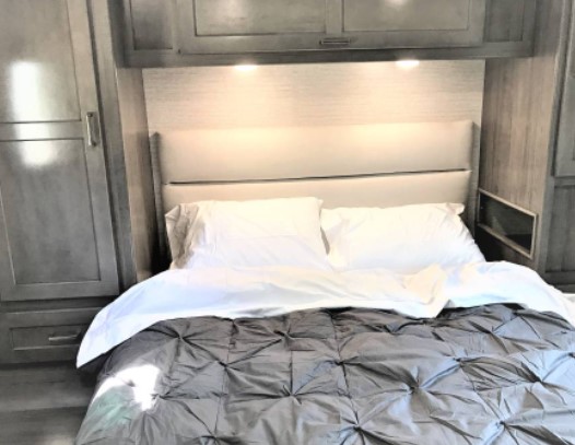 Cozy RV rental bedroom with modern grey interior, bright headboard lighting, and ample storage for comfortable travel.. Winnebago Minnie Winnie 2020
