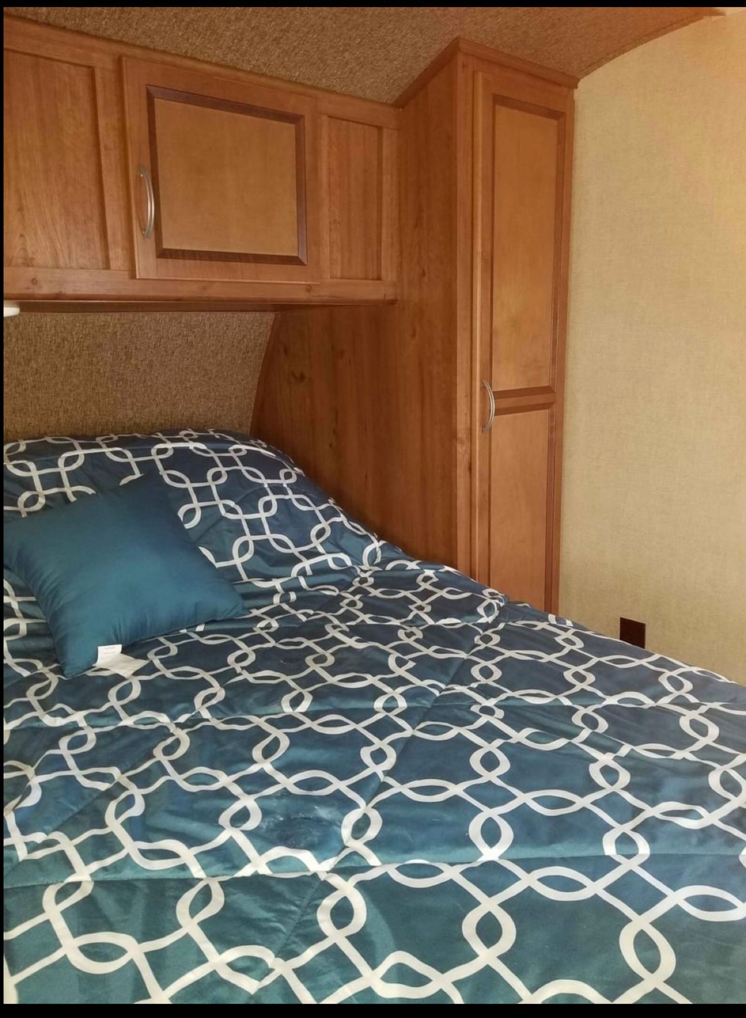 An RV rental bedroom showcasing a patterned bed, overhead cabinets, and a tall wardrobe for storage.. Gulf Stream Innsbruck 2017