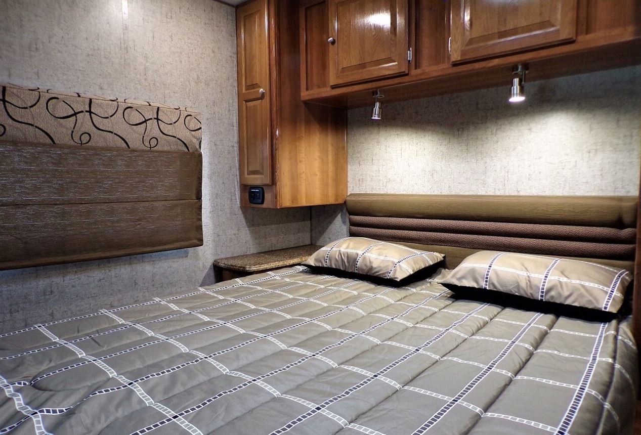 Cozy RV rental bedroom interior with a comfortable bed, patterned comforter, overhead cabinets, and reading lights.. Coachmen Leprechaun 2018