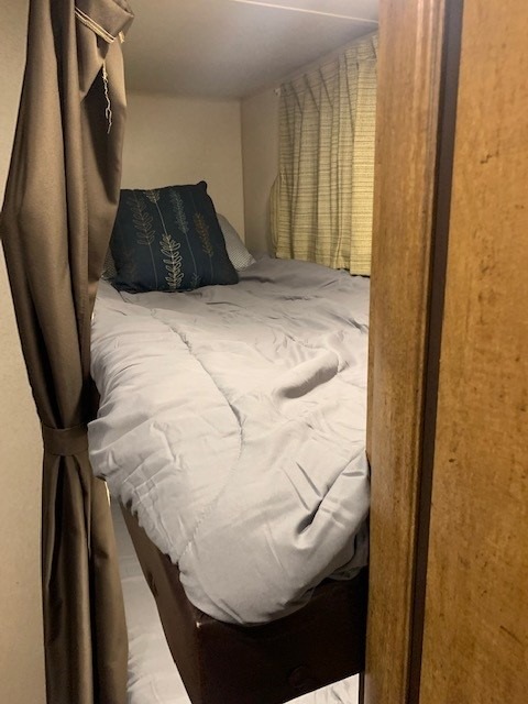 Cozy RV rental bunk bed features a grey comforter, patterned pillow, and side privacy curtain for travel comfort.. Forest River Wildwood X-Lite 2017