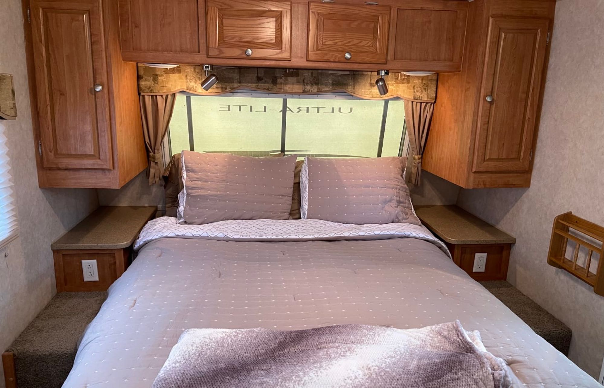 Cozy RV rental bedroom showing a comfortable bed, overhead wooden cabinets, and practical bedside tables for your travels.. Forest River Rockwood Ultra Lite 2009