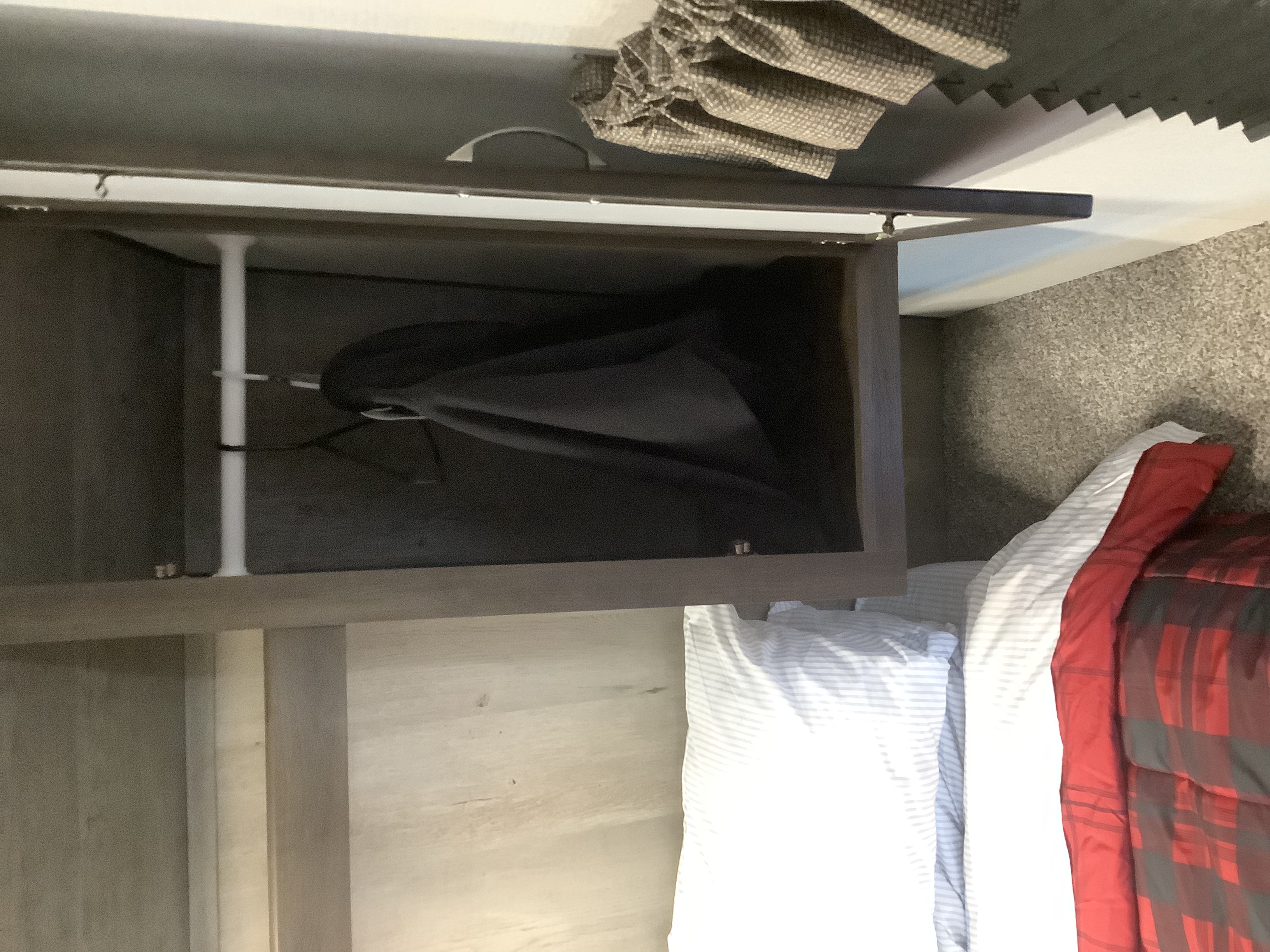 Open overhead storage in an RV rental bedroom, with a laundry bag, white support, and cozy red plaid bedding.. Other Other 2020