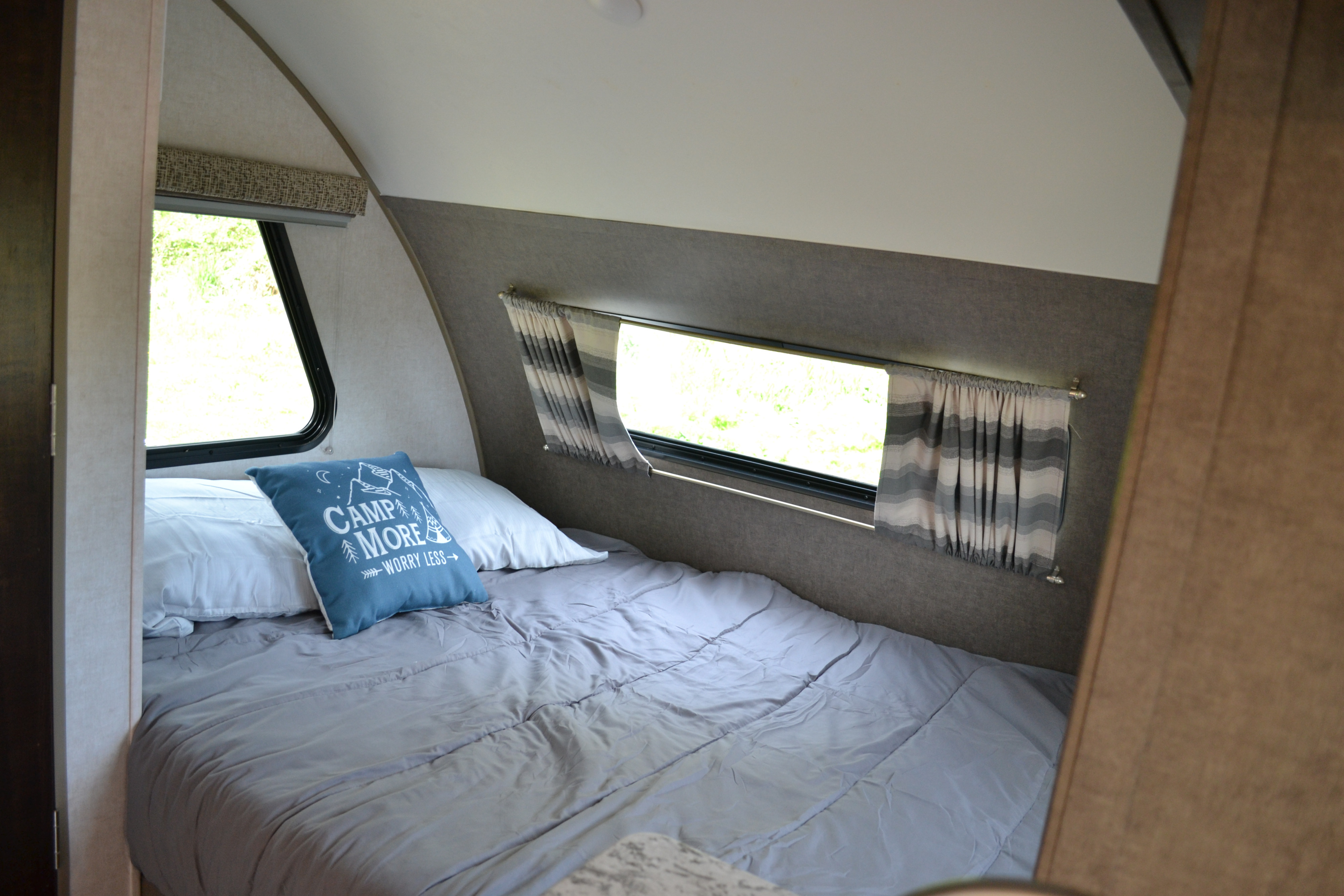 Comfortable sleeping area inside an RV rental, with a tidy grey bed, decorative pillow, and sunlit windows.. R-Pod R177 2018